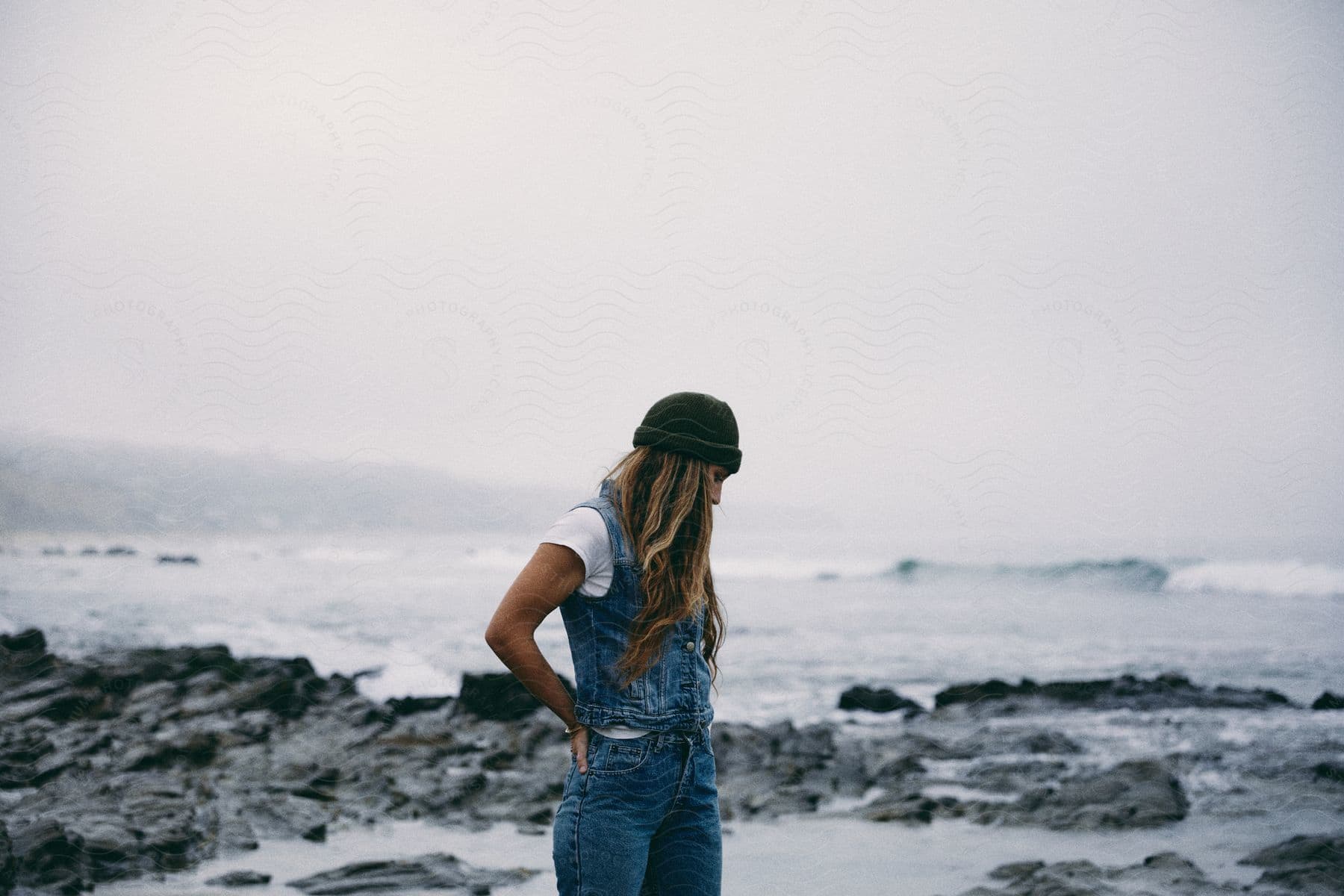 A confident lady stands among rocky water land wearing casual jeans that exude freedom and adventure