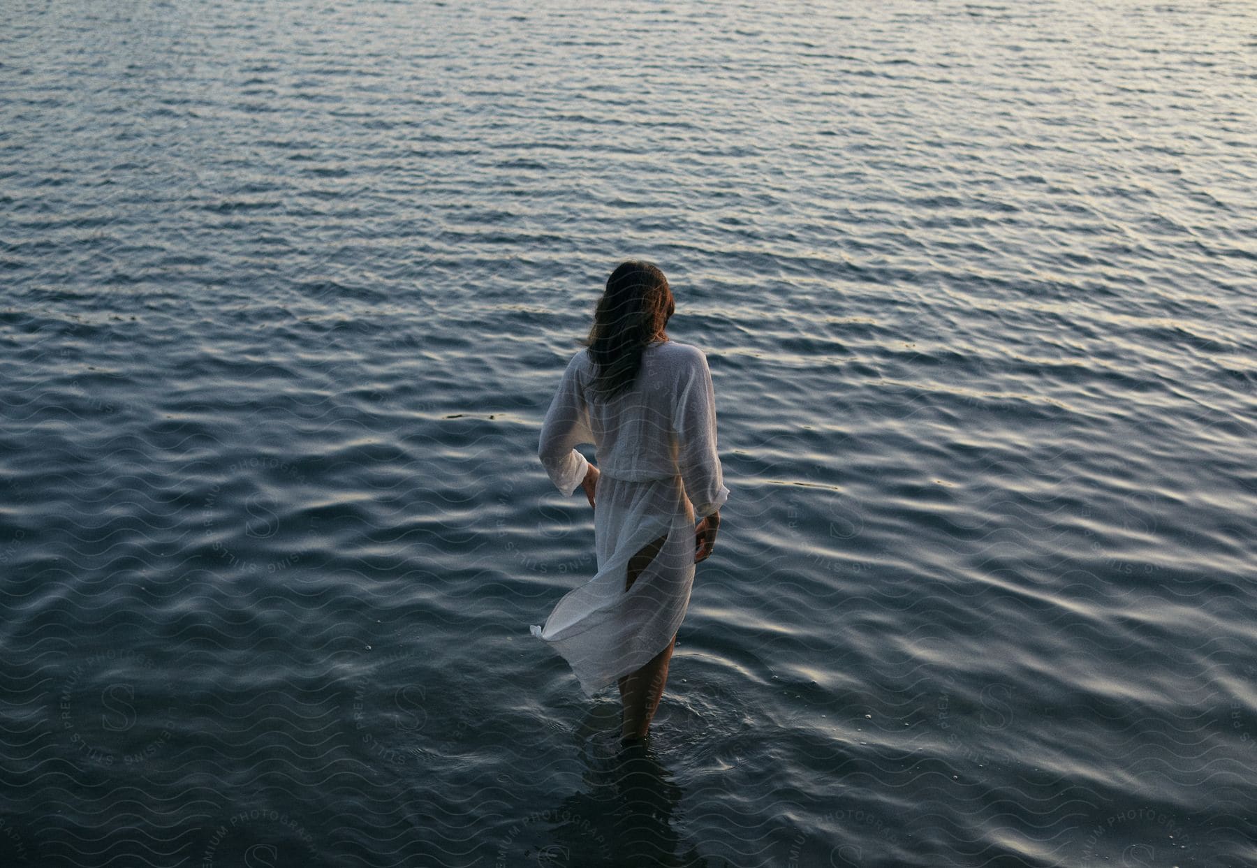 A woman standing near a lake at dusk