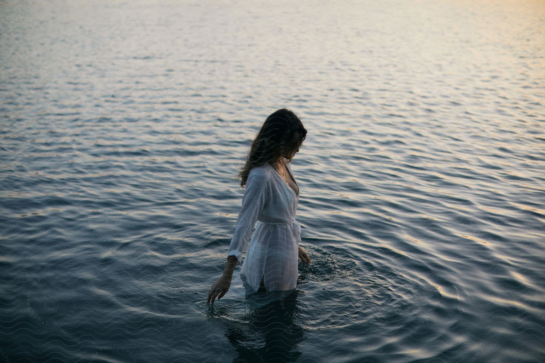 A woman in a white dress standing in water with sunlight shining on ripples