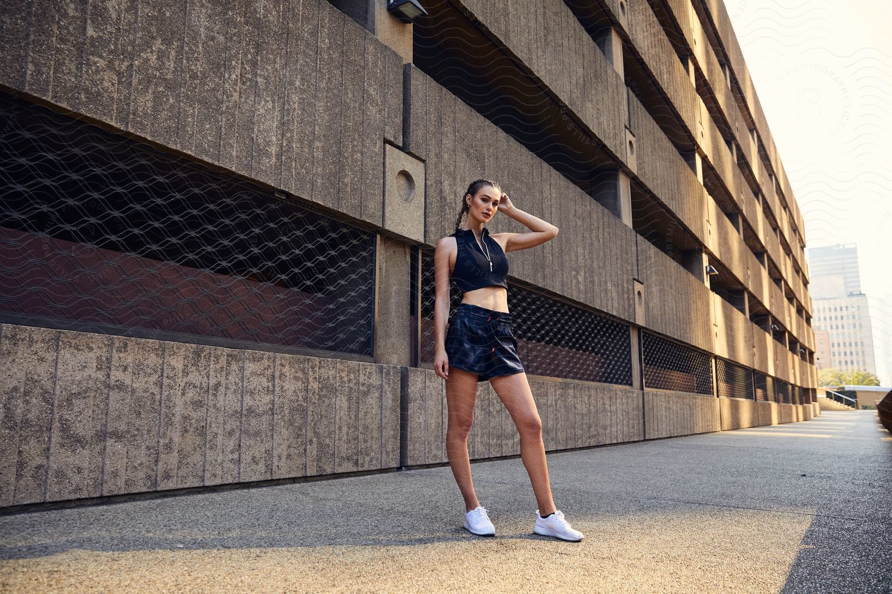 A woman with braided hair stands next to a downtown building showcasing her fashionable outfit