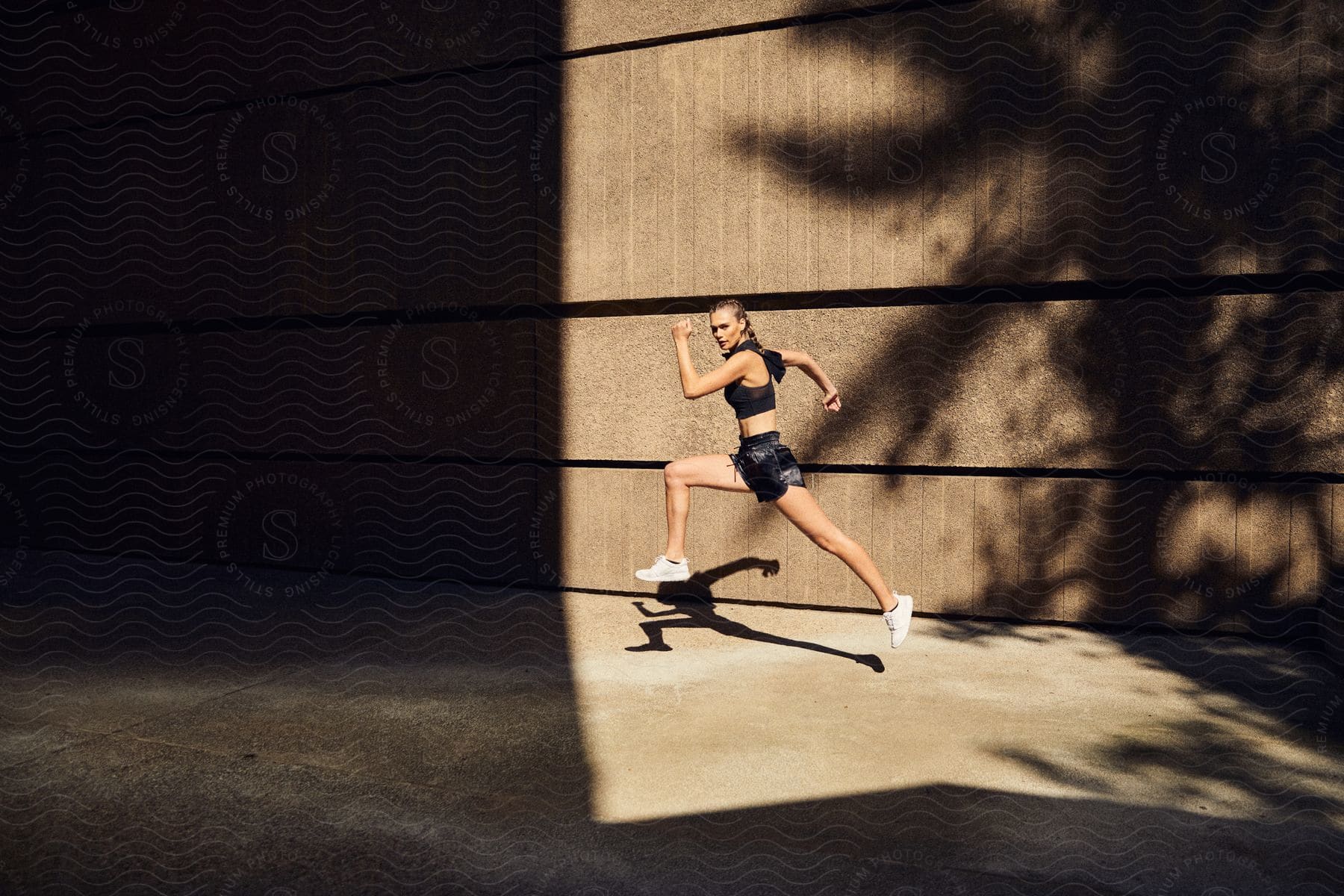 A person wearing shorts and running shoes is captured in a flash photography shot with a wooden background holding sports equipment and performing a kickflip