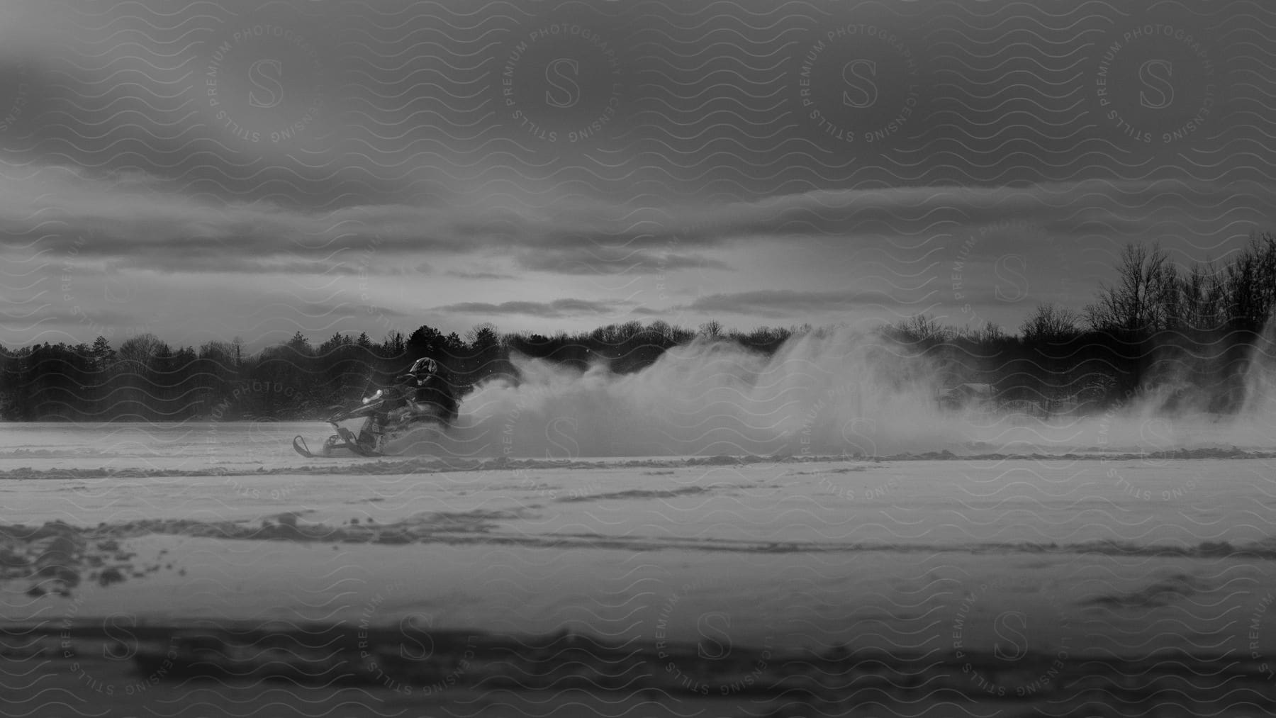 A snowmobiler drives through the snow creating a cloud of snow behind them