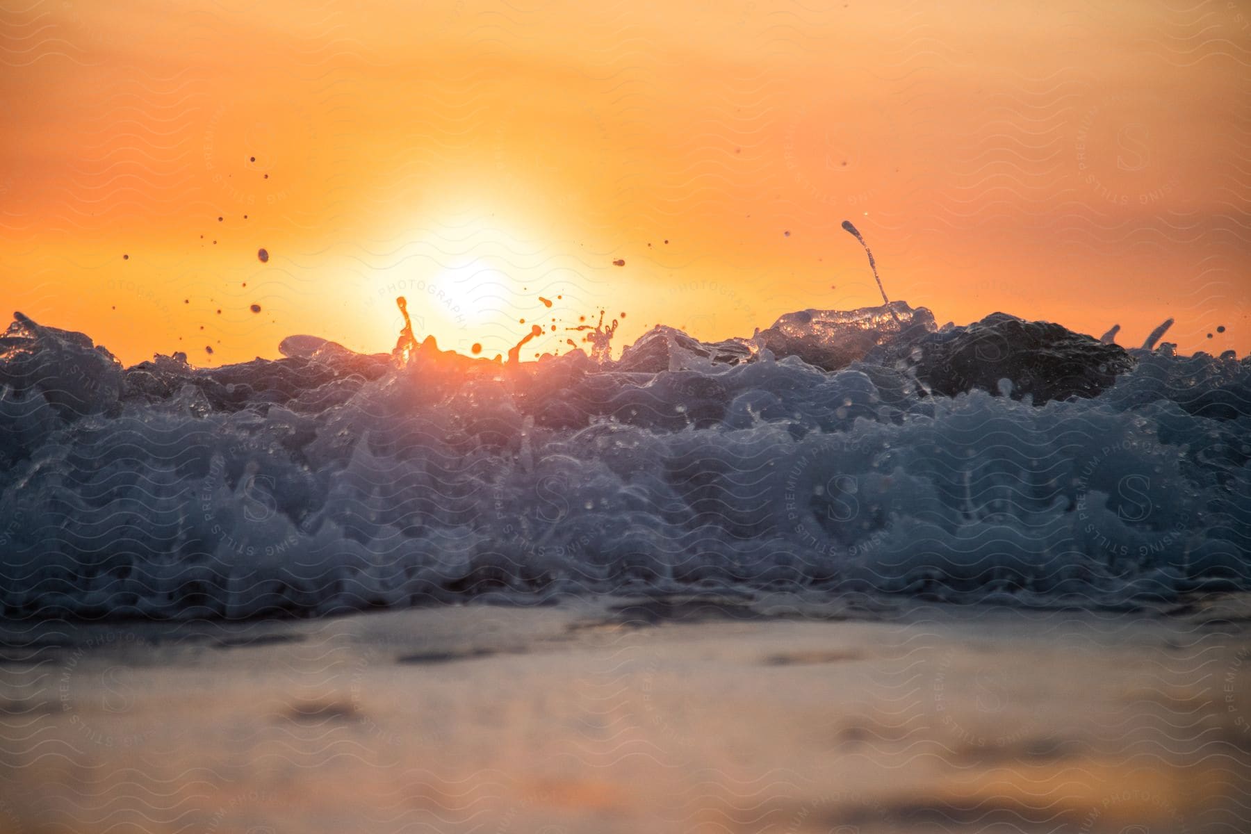 Sun shining over ocean wave breaking against the shore at hazy sunrise by the sea