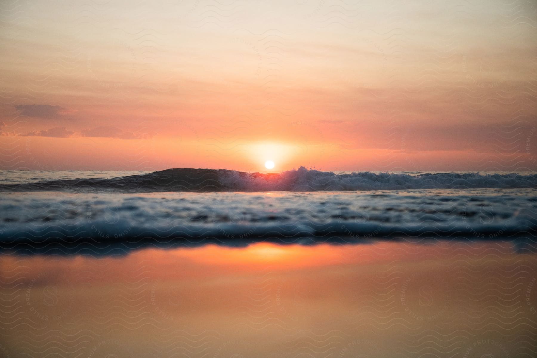 Vibrant colors paint the sky as a massive wave crashes against the sandy beach at sunset