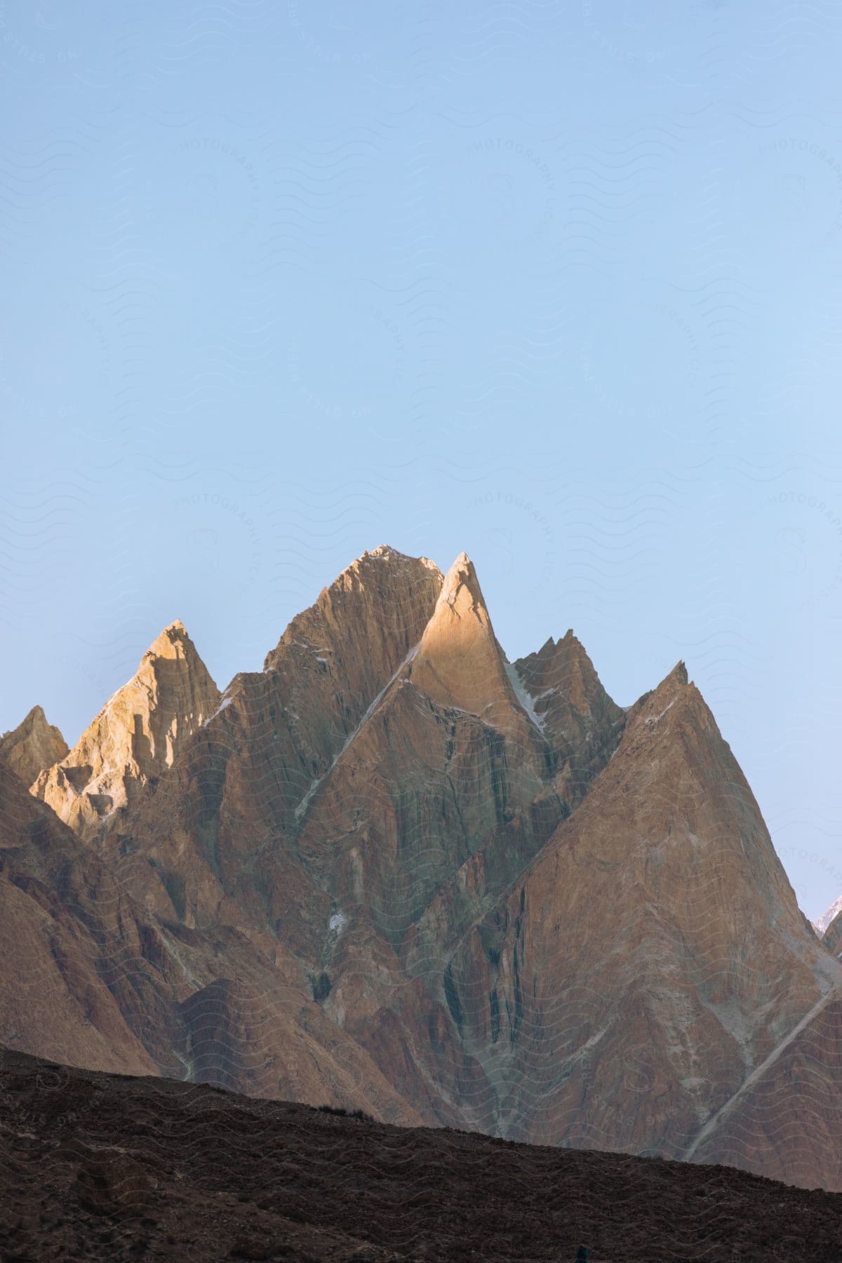 A mountain landscape with a clear sky showcasing a range of peaks and slopes made of brown bedrock