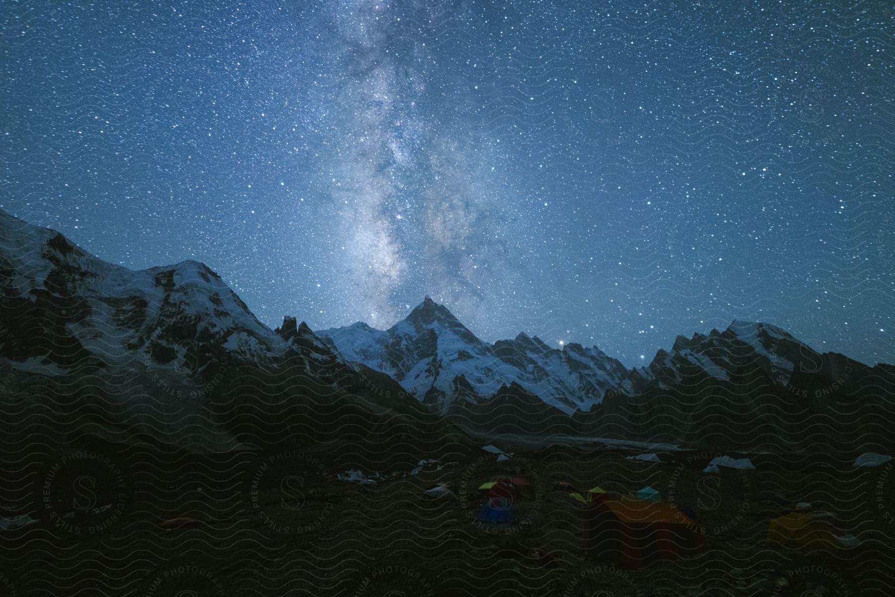 Tents Pitched At The Base Of Snowy Mountains Beneath The Milky Way