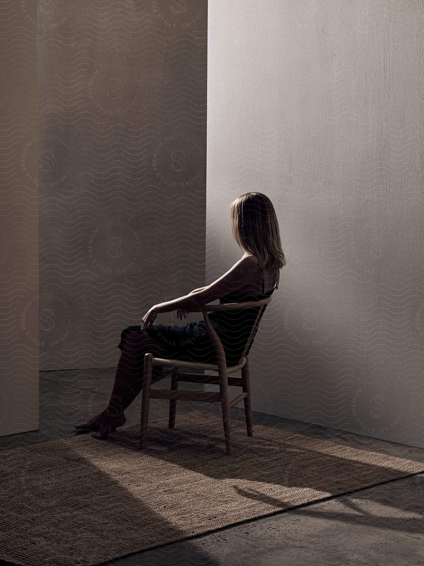 Blonde Woman Sitting In A Chair On A Carpet Near A Wall