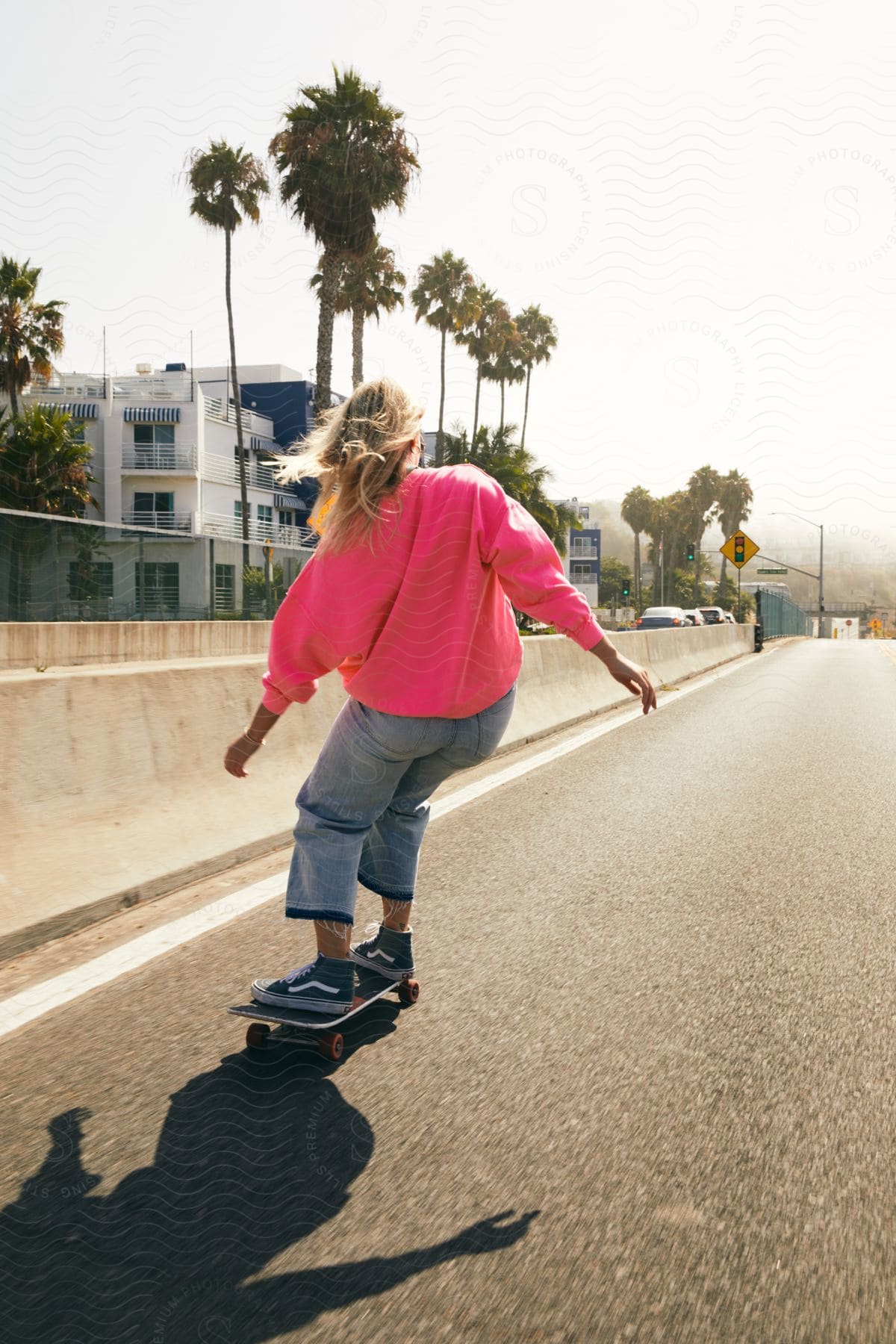 A teenage girl skateboards on a street near apartments as traffic moves across the median barrier