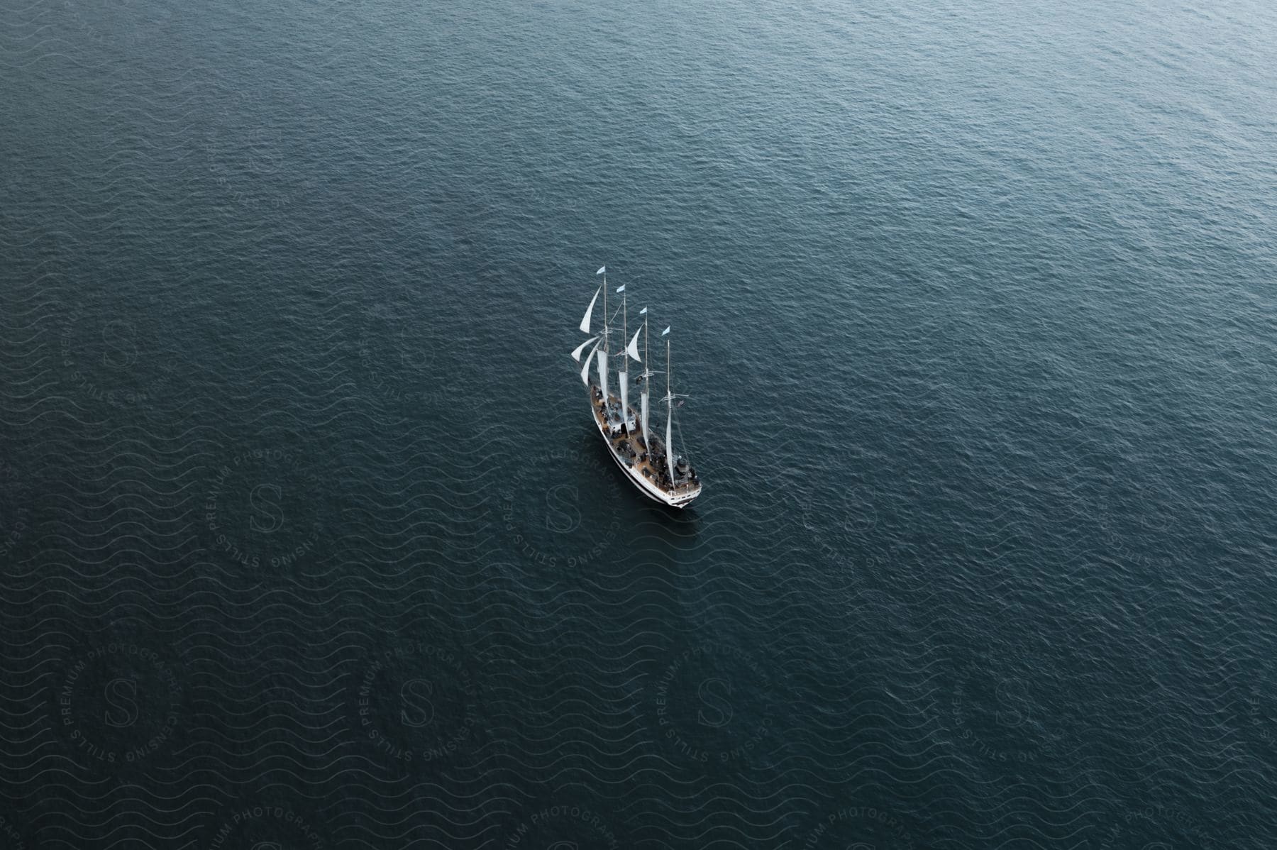 A sailboat with a white flag sails alone in the dark blue ocean