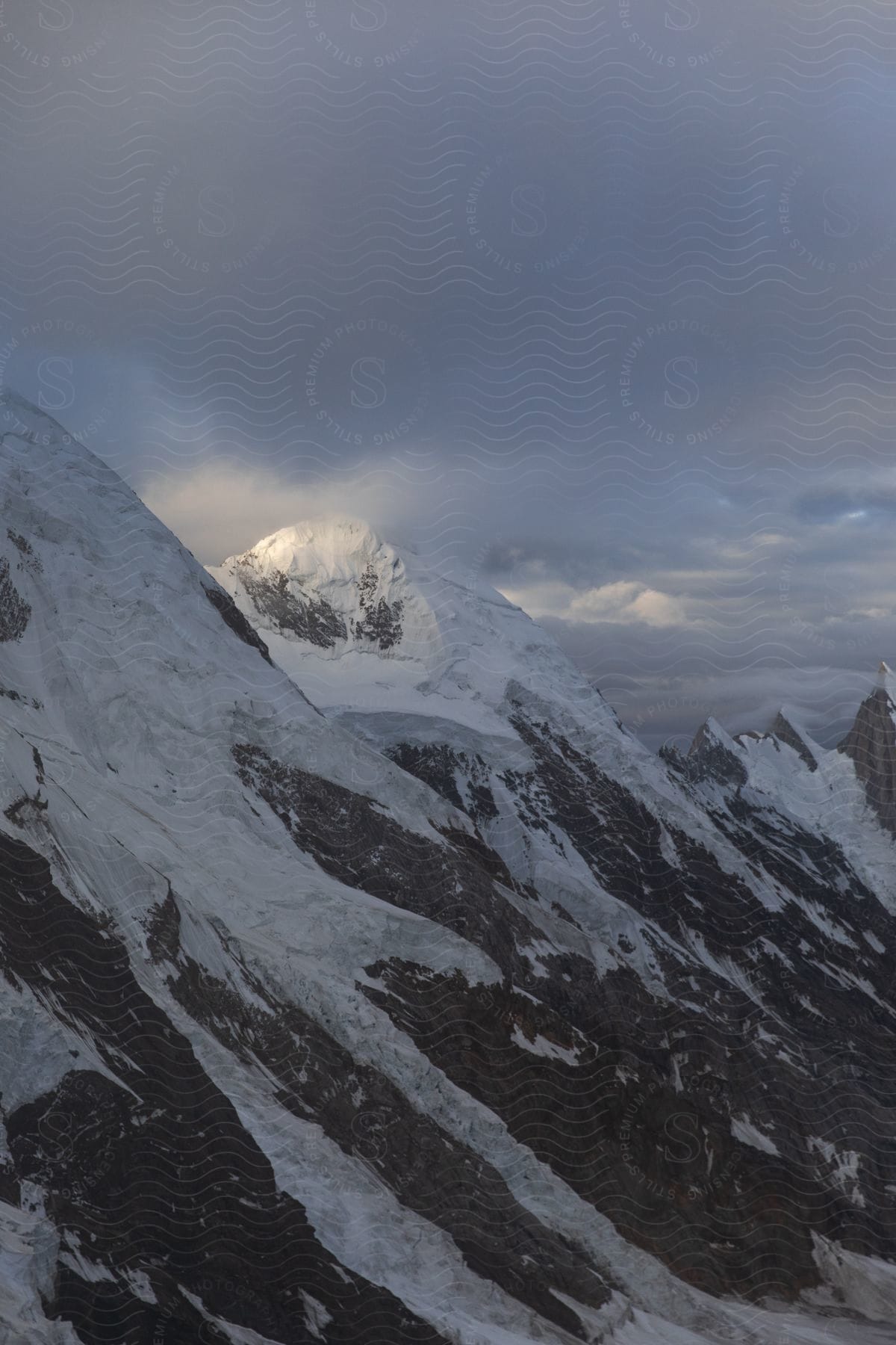 Snowcapped mountains with a peak highlighted by the sun peeking through the clouds in the himalayan mountain range