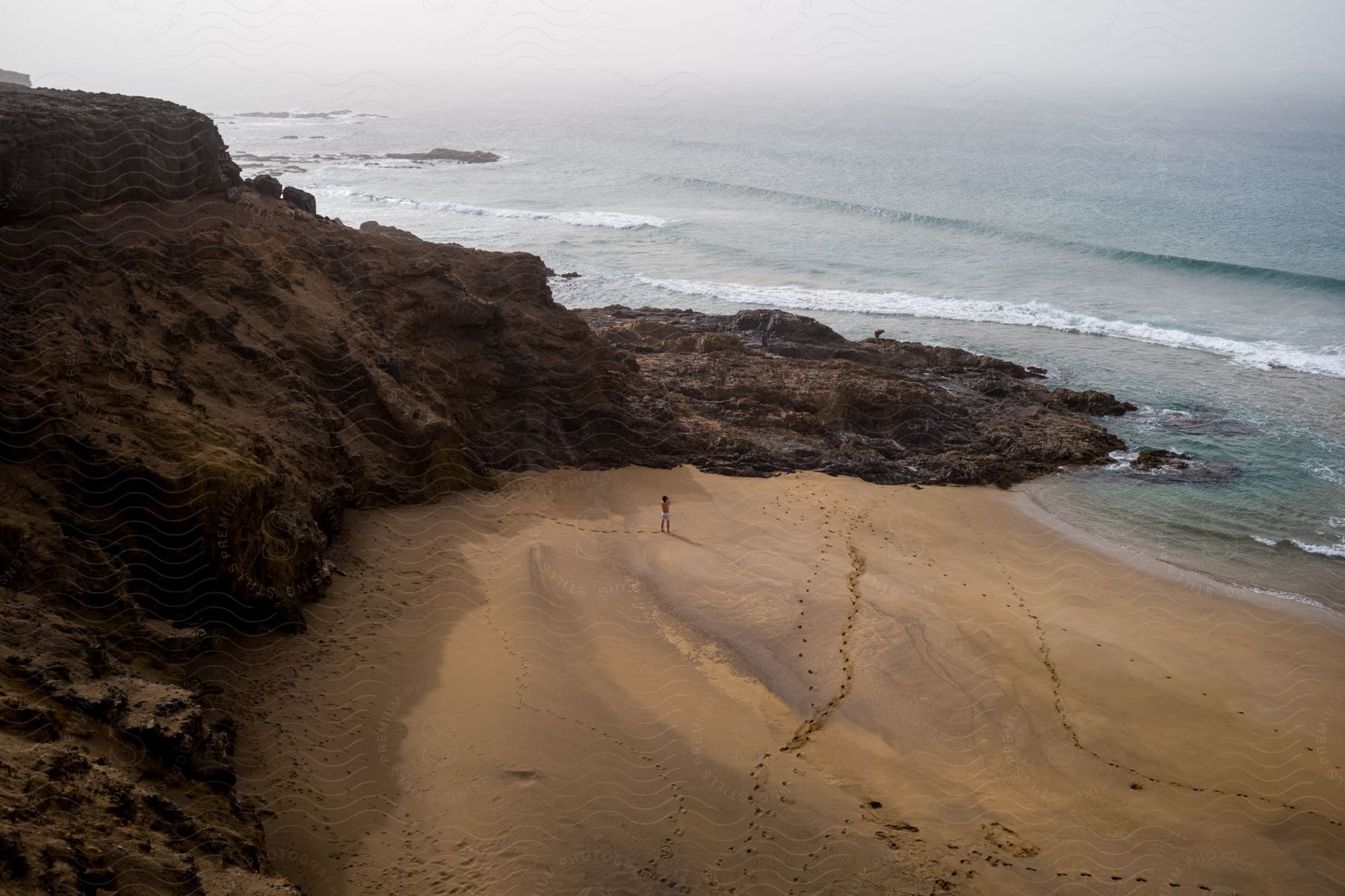 A person stands alone on a rocky shoreline looking out at the sea