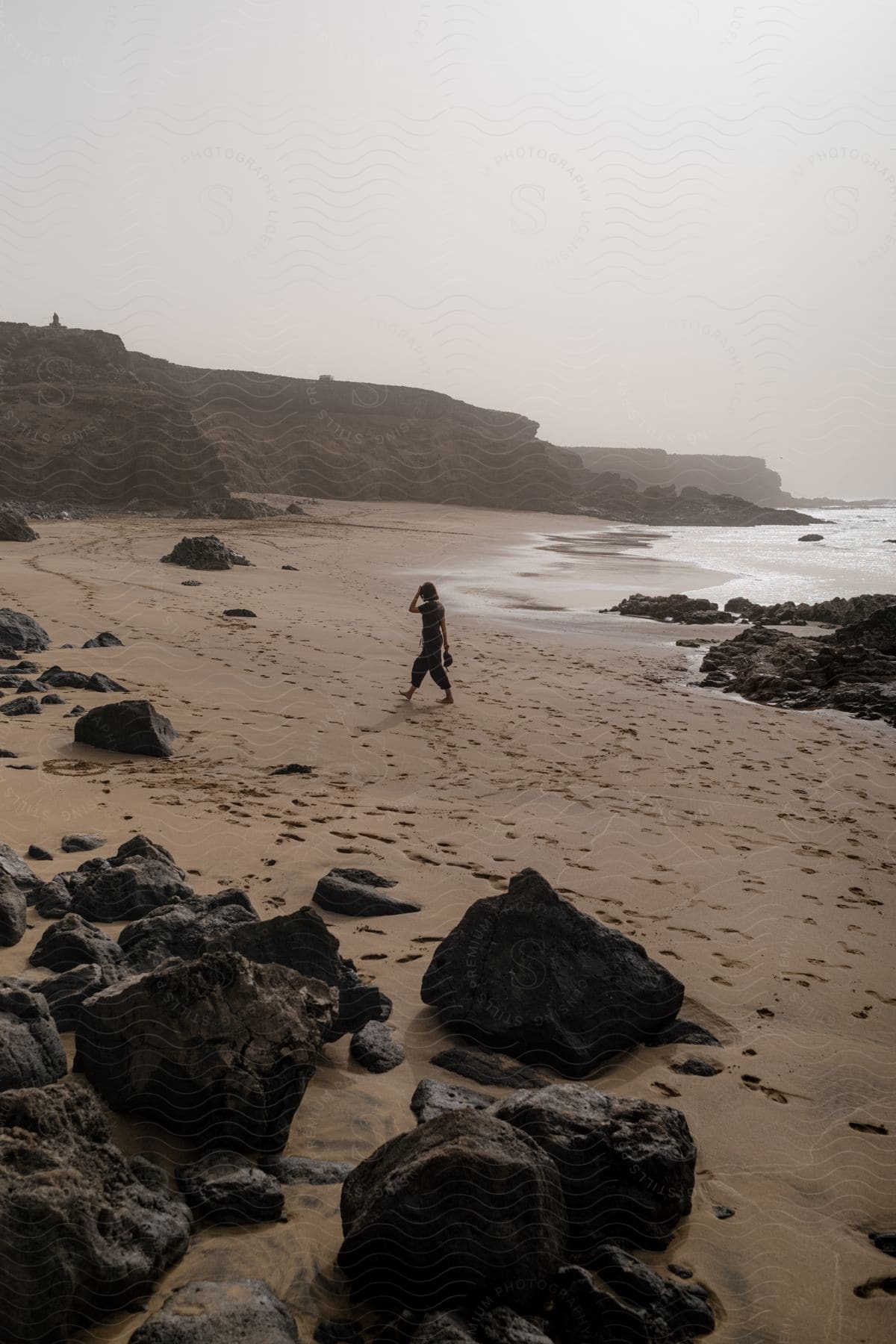 Person walking along a rocky beach on a hazy day