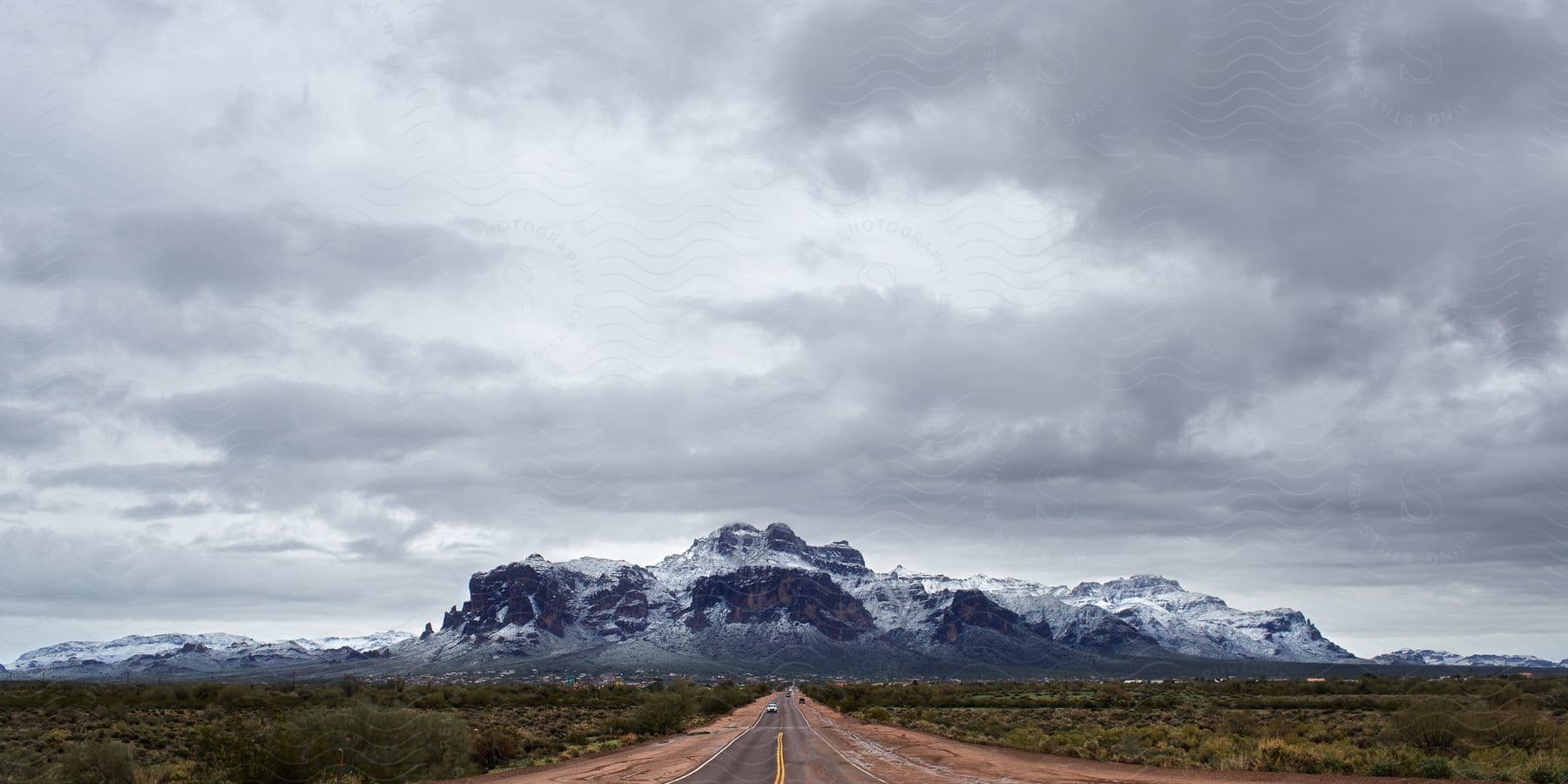 A long road with greenery on the side and snowy mountains in the background