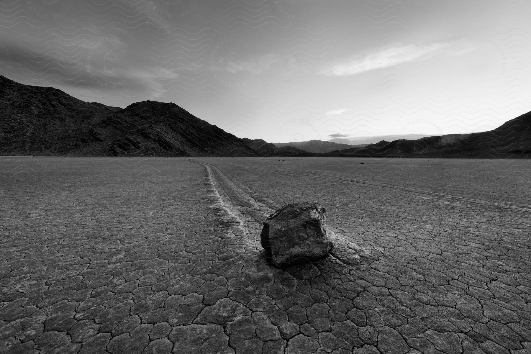 A sailing stone leaves a trail in the desert soil next to the mountains at evening