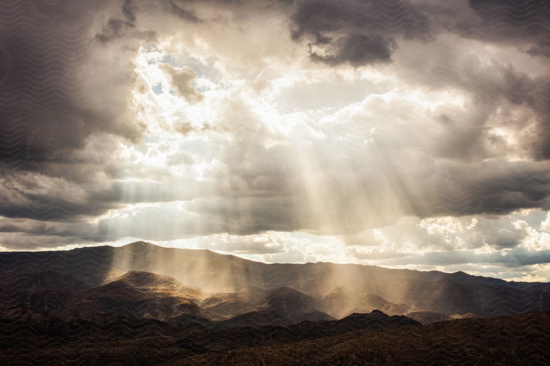 Light beams shine through a gap in the clouds in a mountainous landscape of rocks