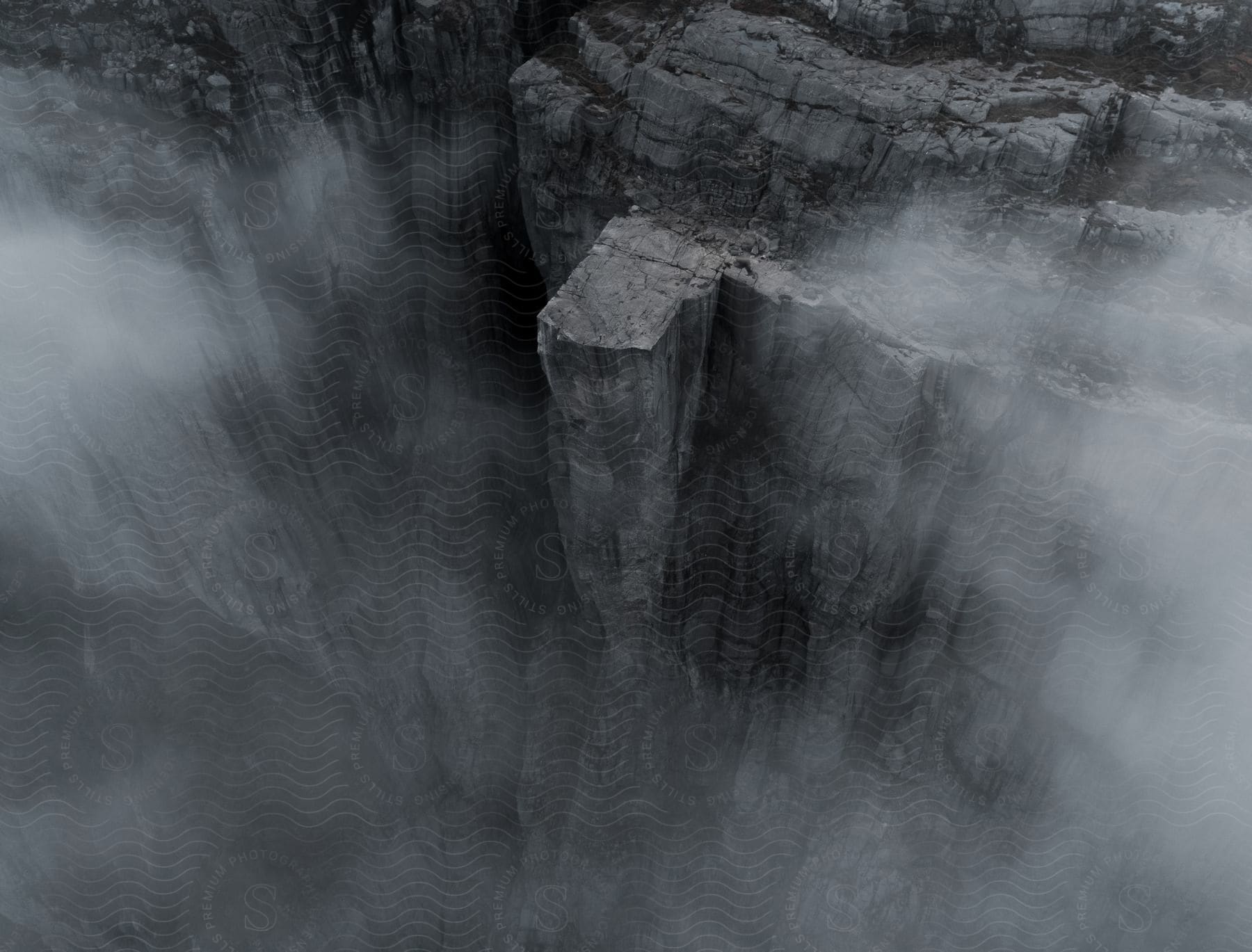 A grey and blackandwhite natural landscape with a waterfall cliff and water