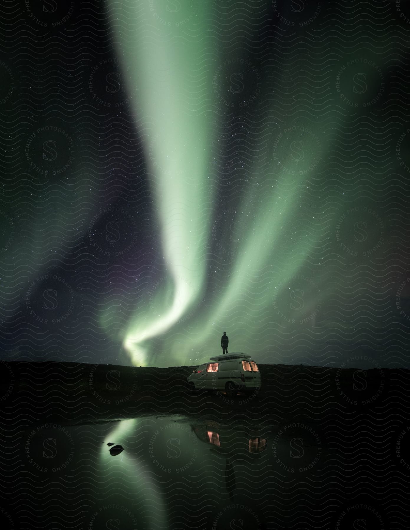 A man stands on a van and stares up at the aurora borealis in the night sky