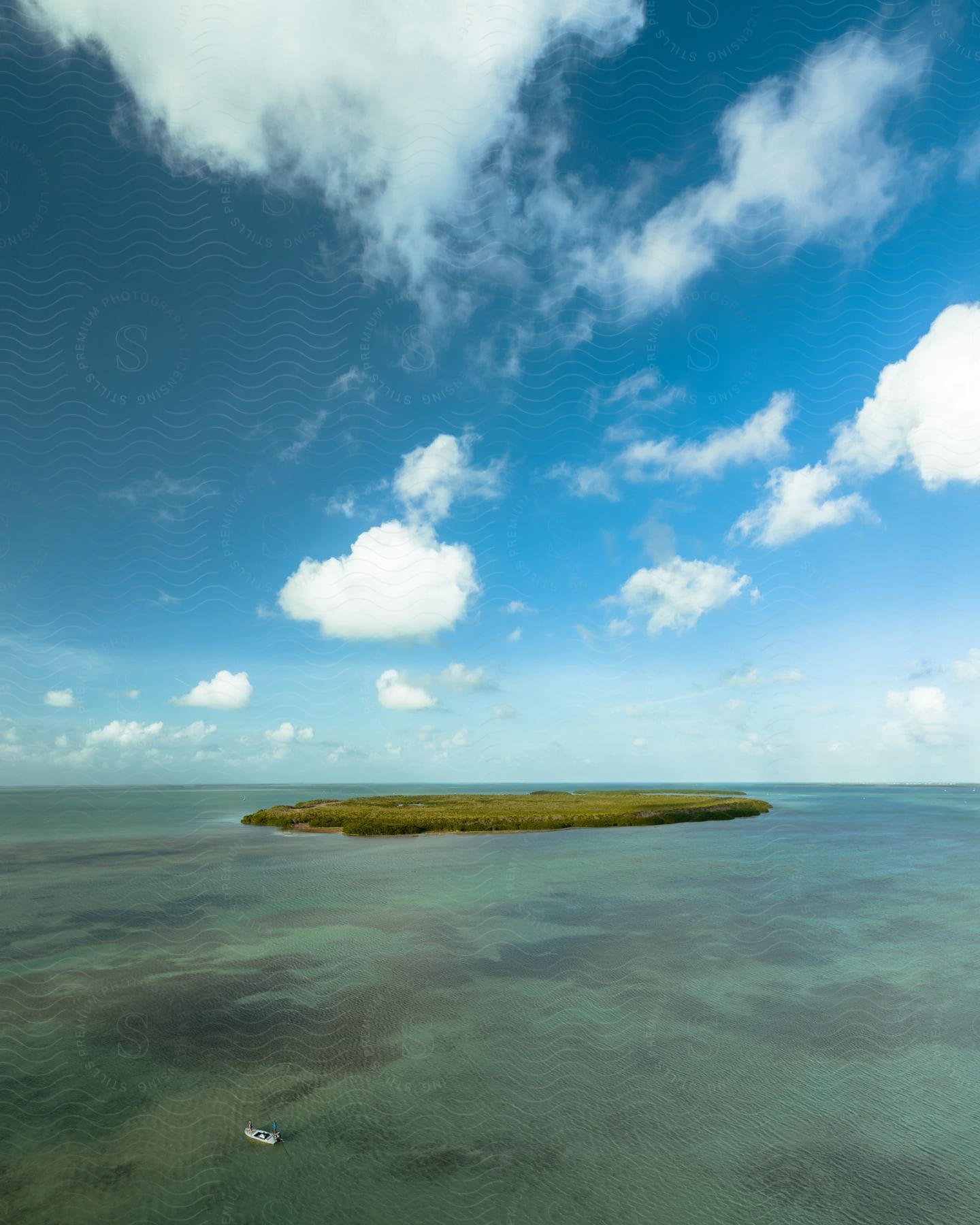 A boat sails near a small island with fluffy cumulus clouds in the blue sky