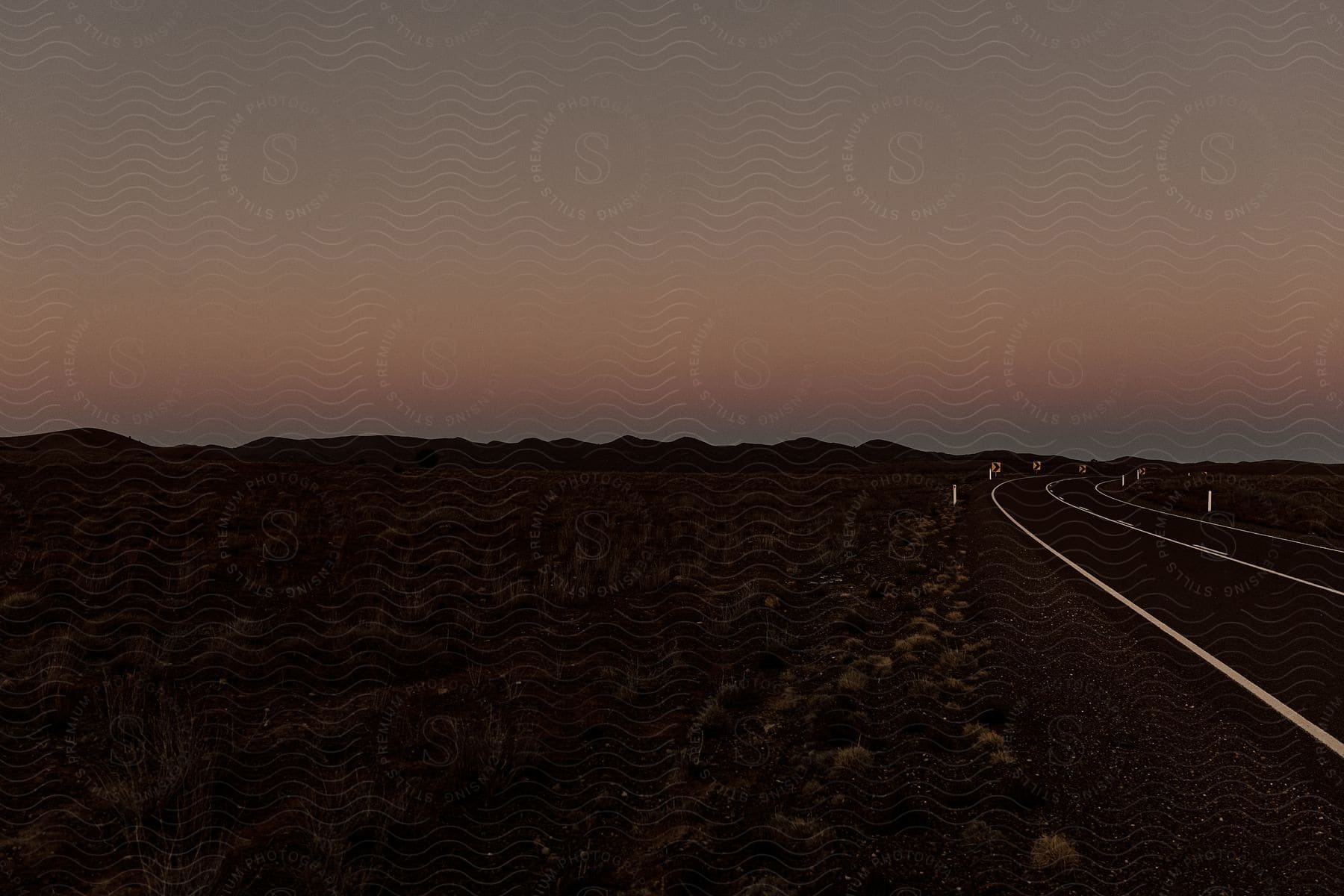 A rural highway at dusk with the sun setting on the horizon