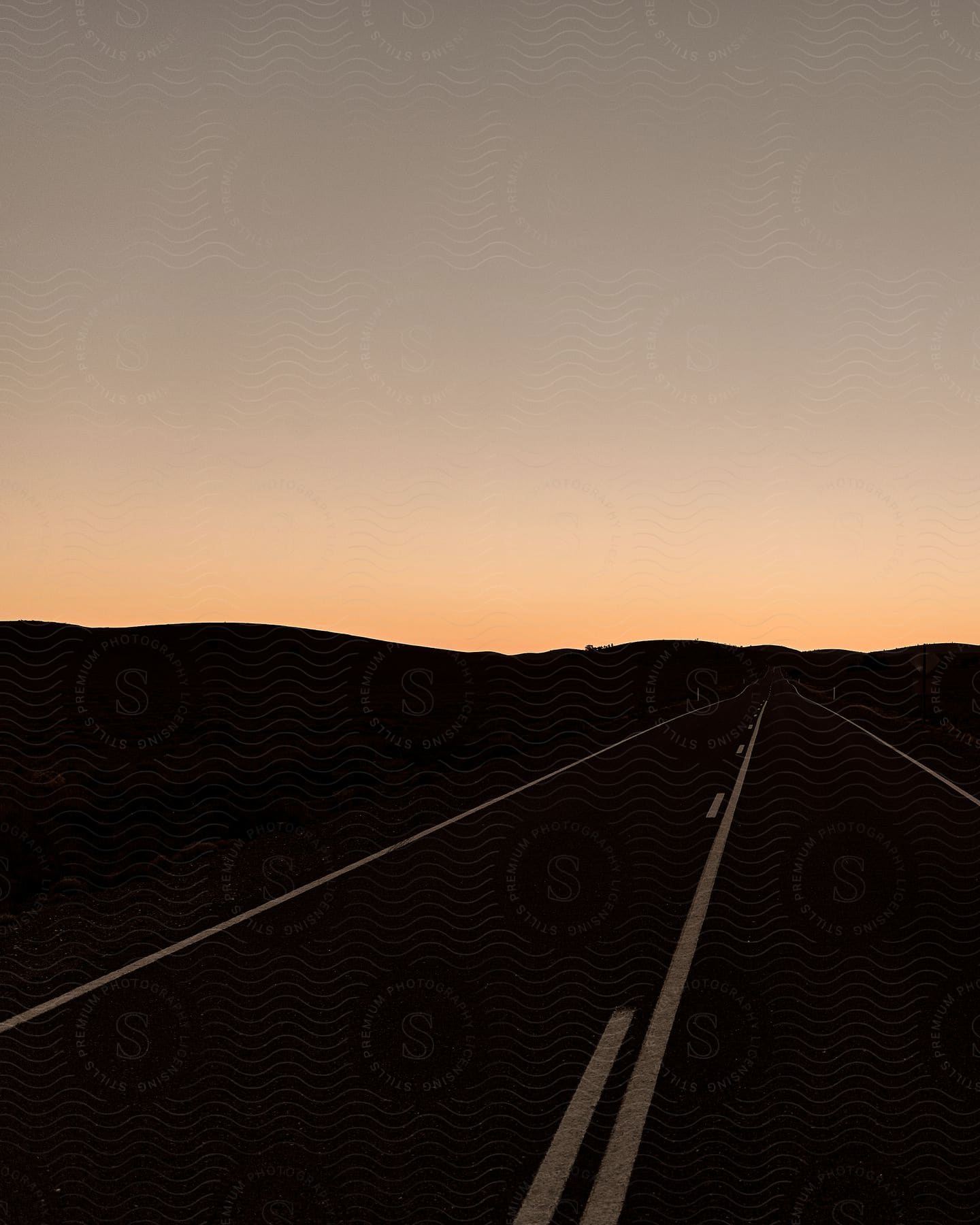 An open highway stretches towards distant hills under a clear sky
