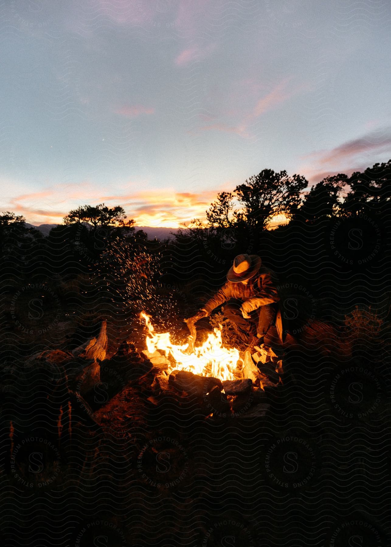 Man sitting near blazing bonfire in field at dusk