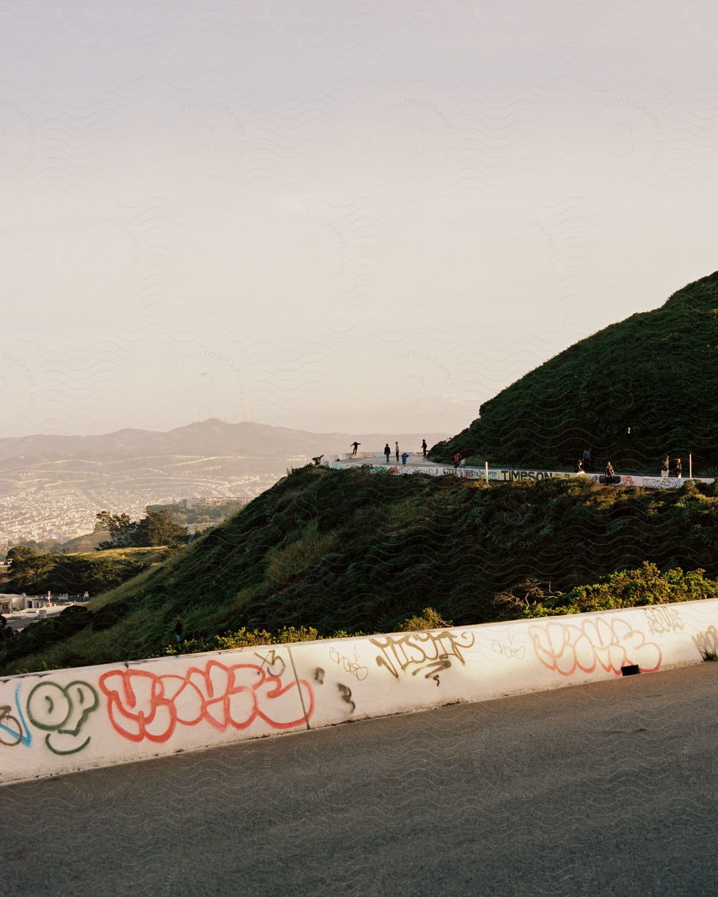 People enjoy a cool autumn day on a twisty road with graffiti skateboarding and a city covered in haze in the distance