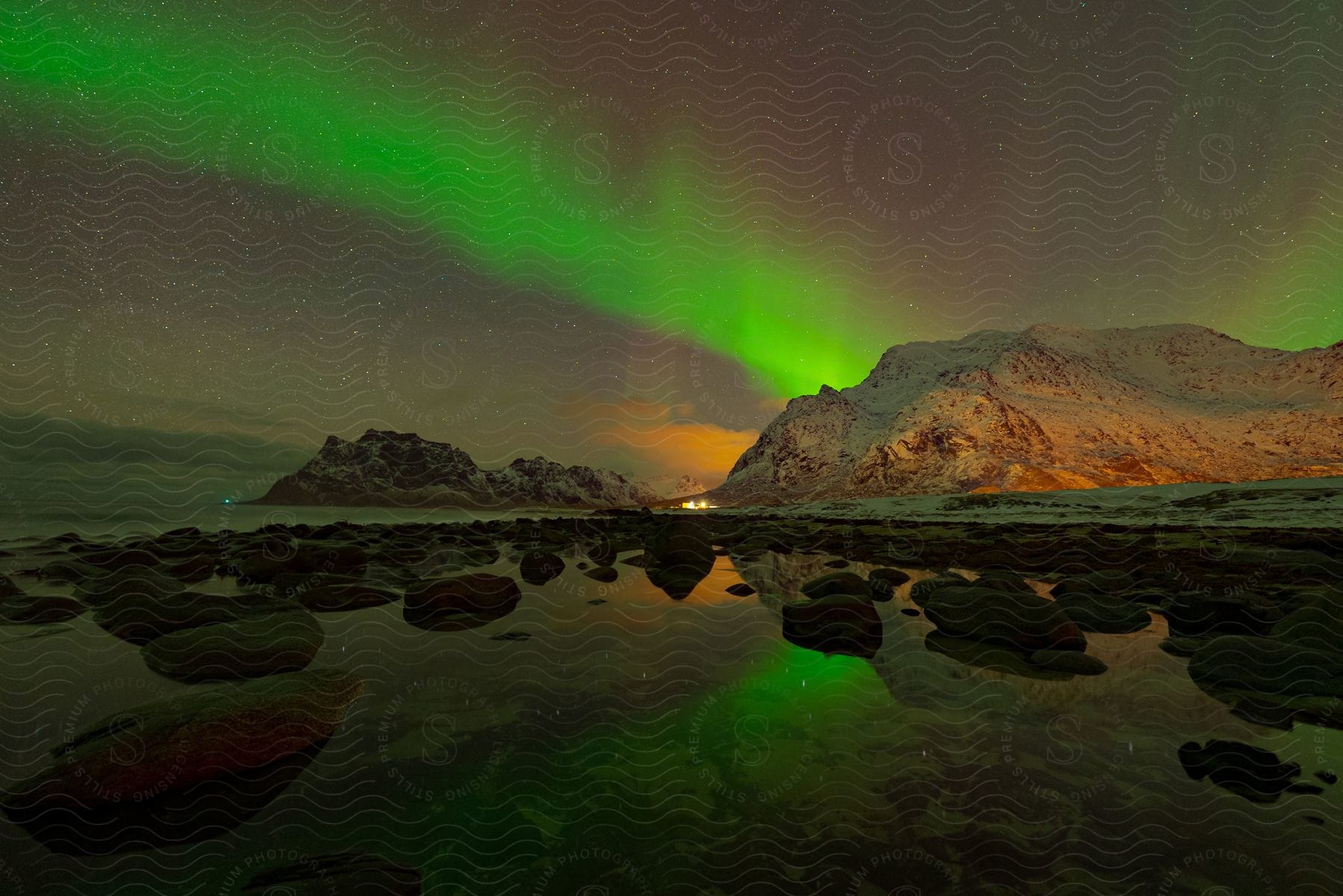 Northern lights reflecting off rocks and water illuminating lakeside cliffs at night in lofoten norway