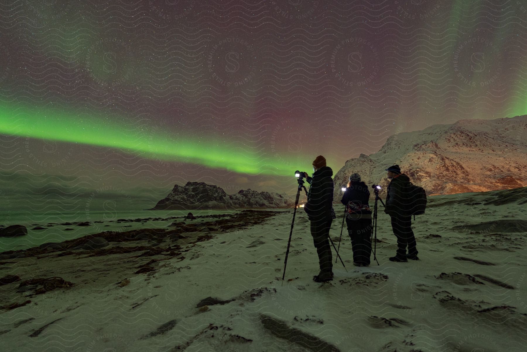 A group of people watching and filming aurora borealis lights in the night sky