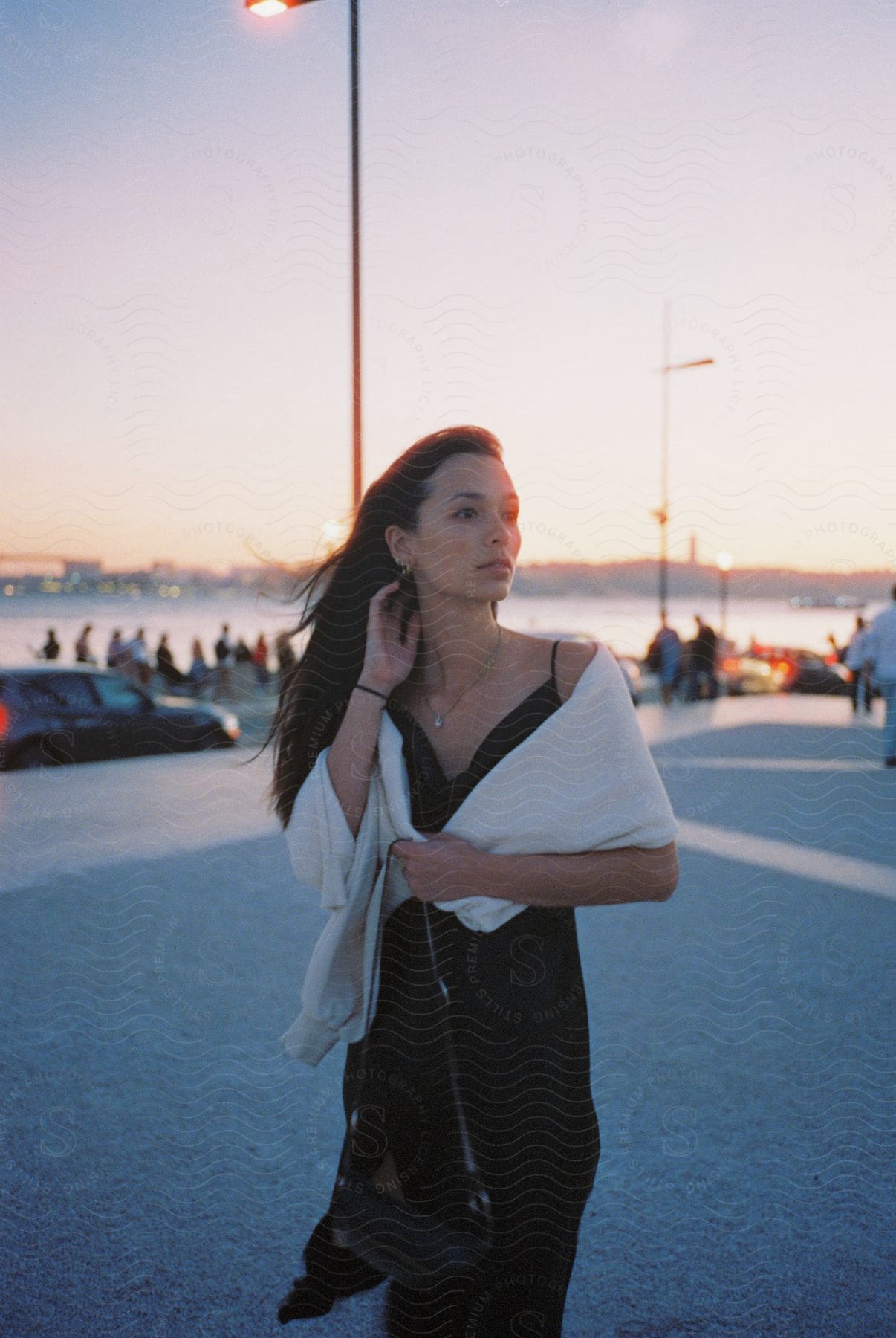 A lady in a black gown stands outdoors at dusk surrounded by blurry images of vehicles and people