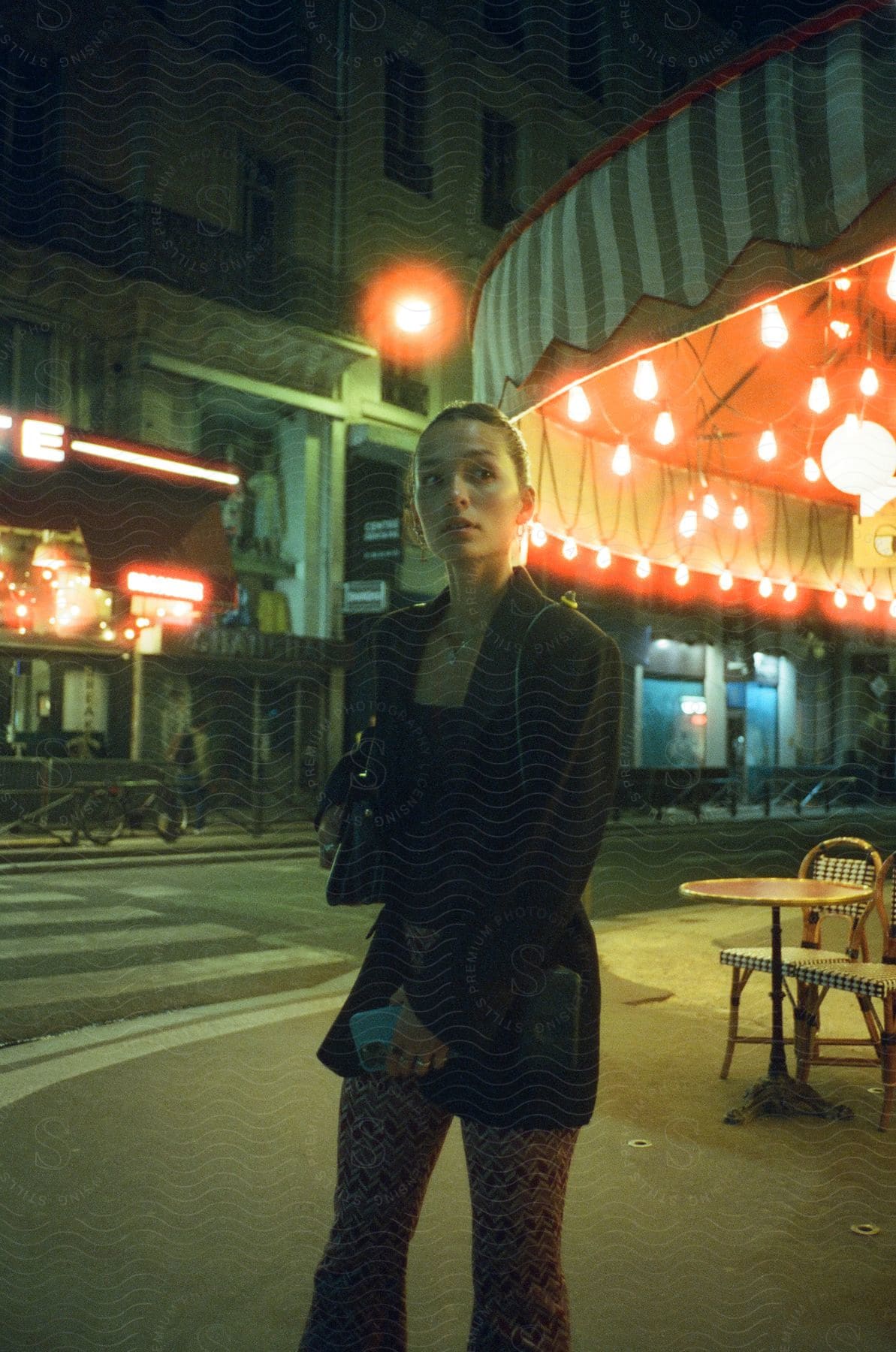 Young woman standing near an outdoor table beside a city street at night time