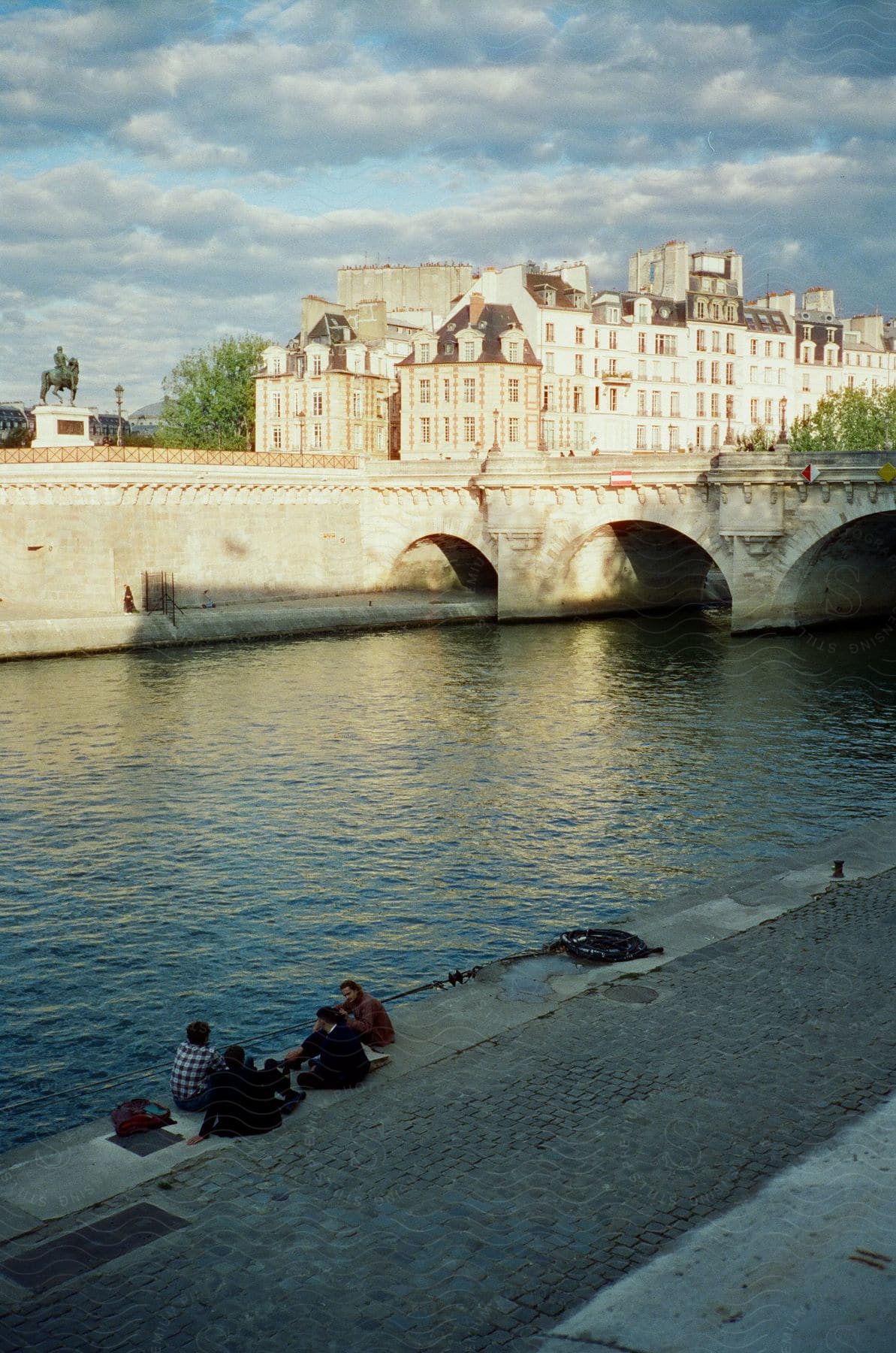 Friends sitting on the bank of a canal across from a statue and historic apartment buildings in paris