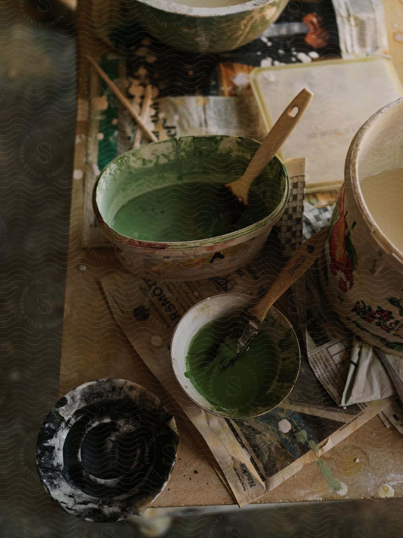 Buckets and bowls of green black and white paint with brushes on a workbench