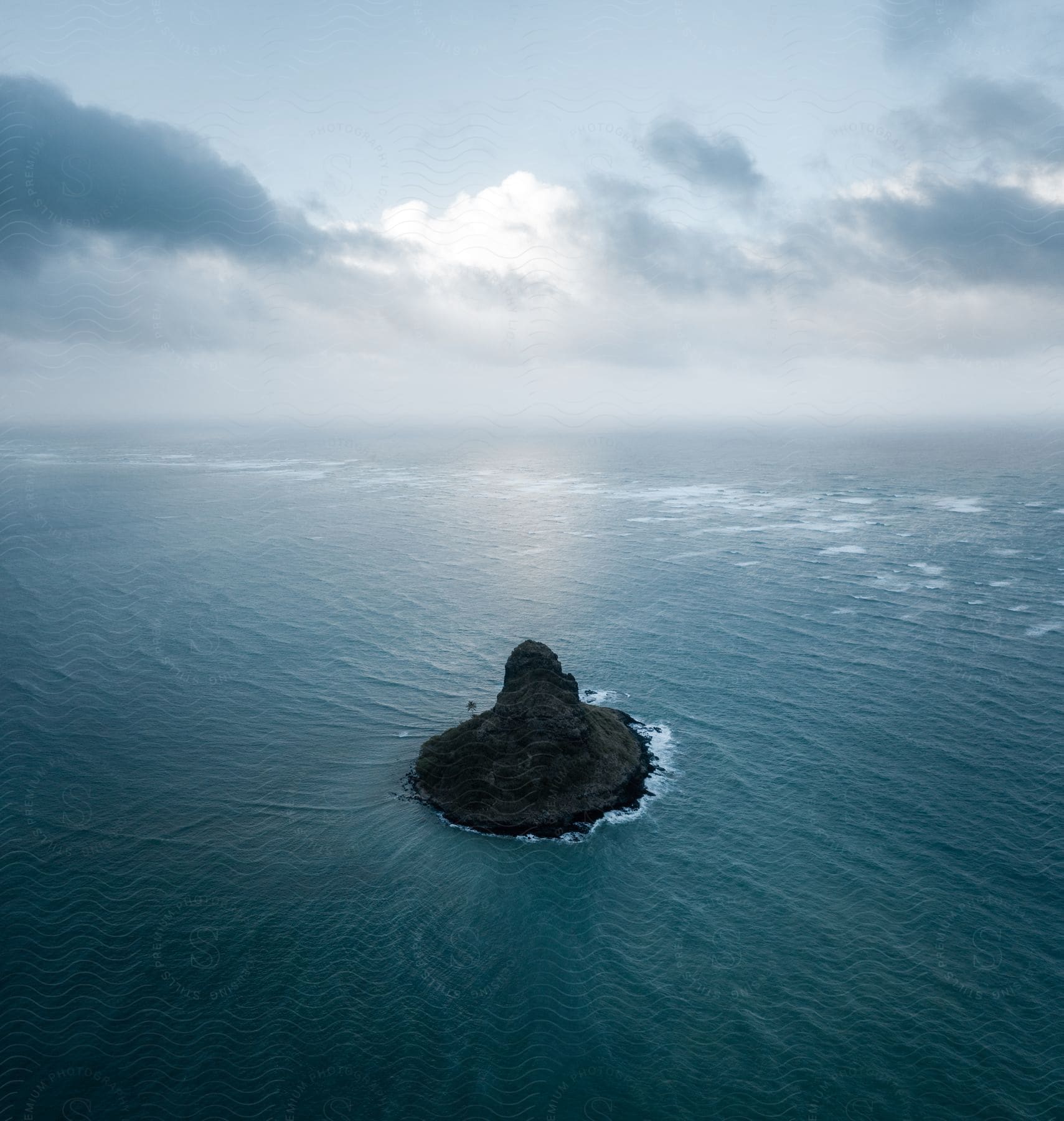 A small island with rock formations is seen in open water under a cloudy sky