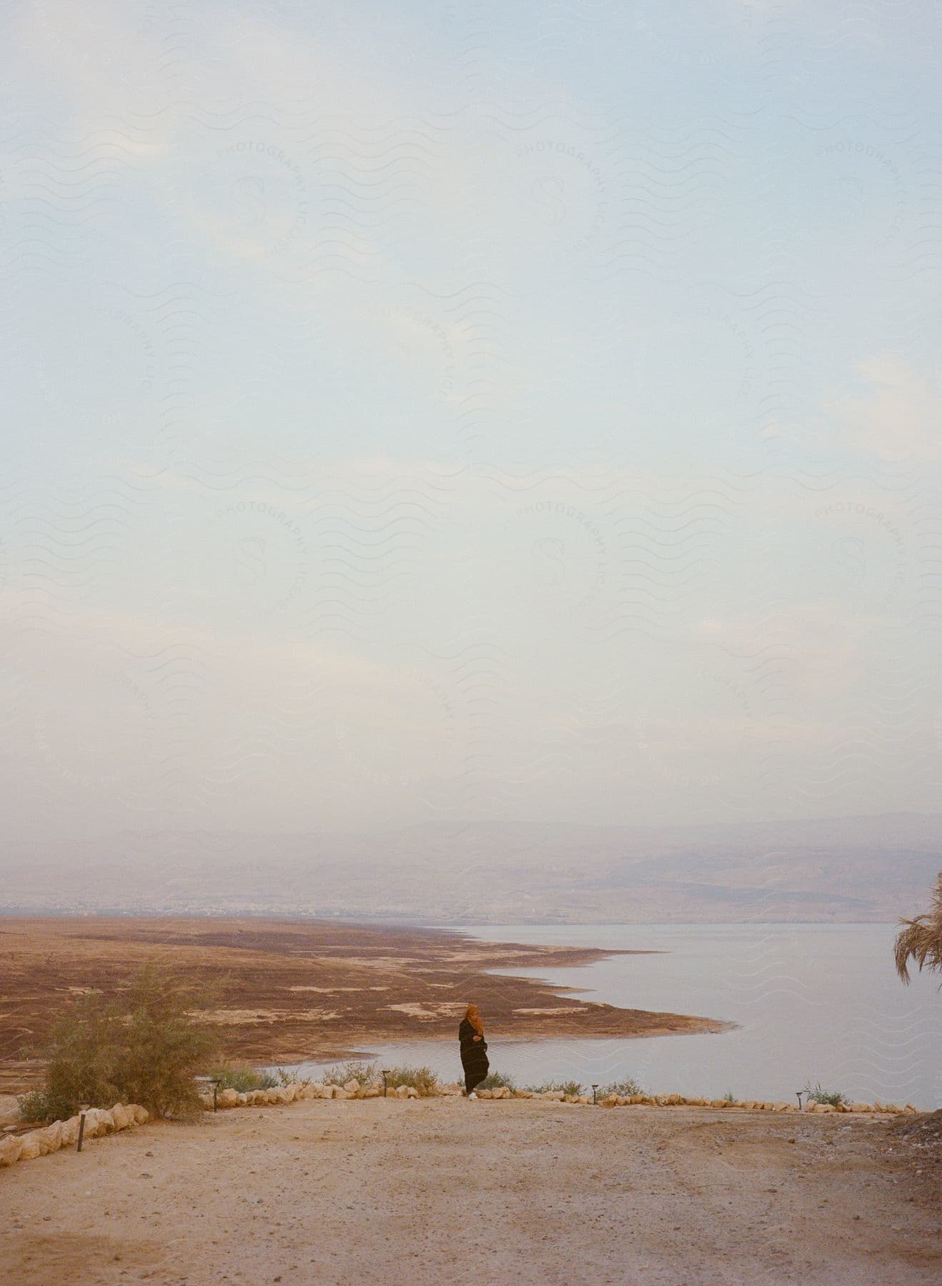 A person standing near a foggy shoreline next to a road and body of water