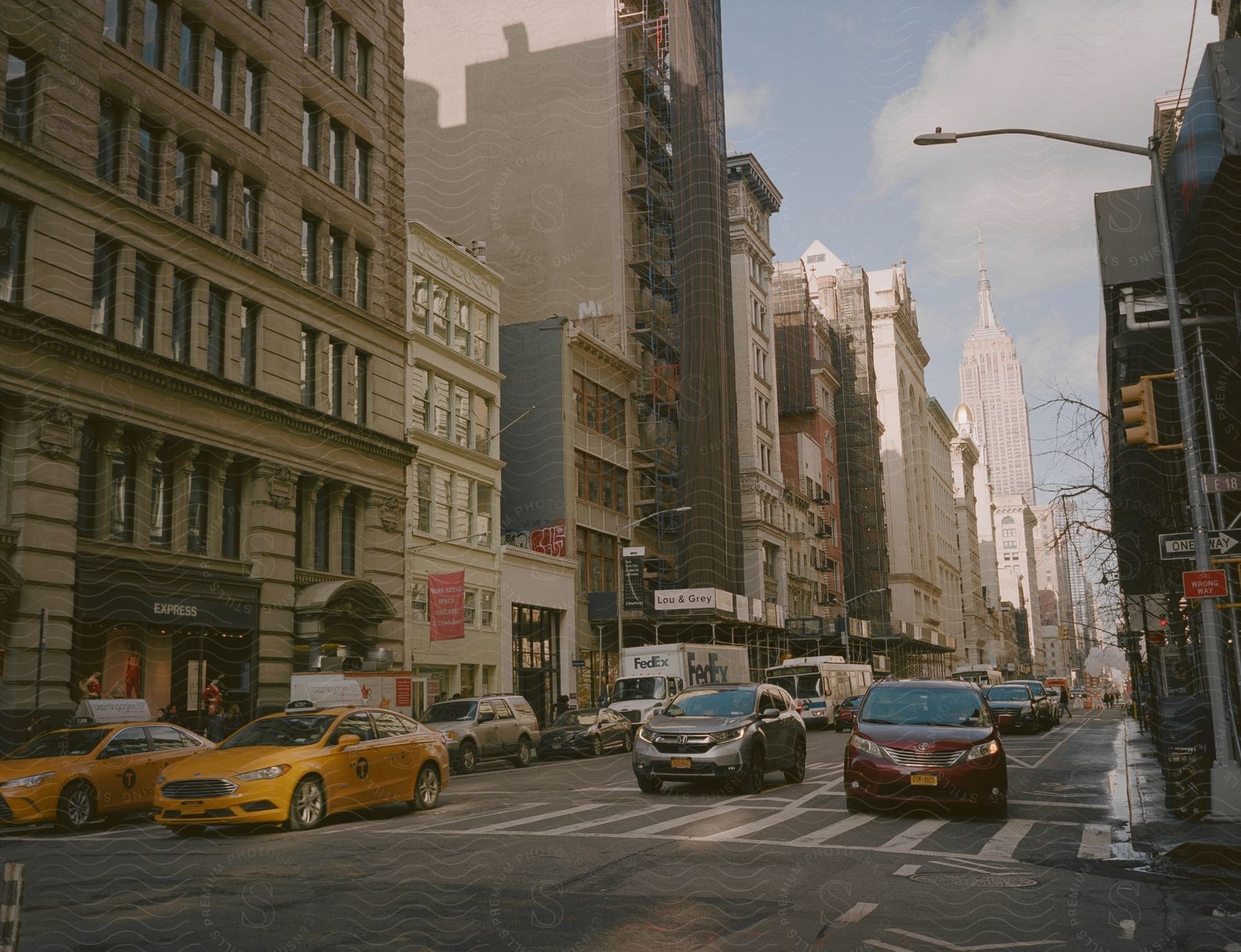 City street with cars driving between tall buildings during the day with sun casting shadows