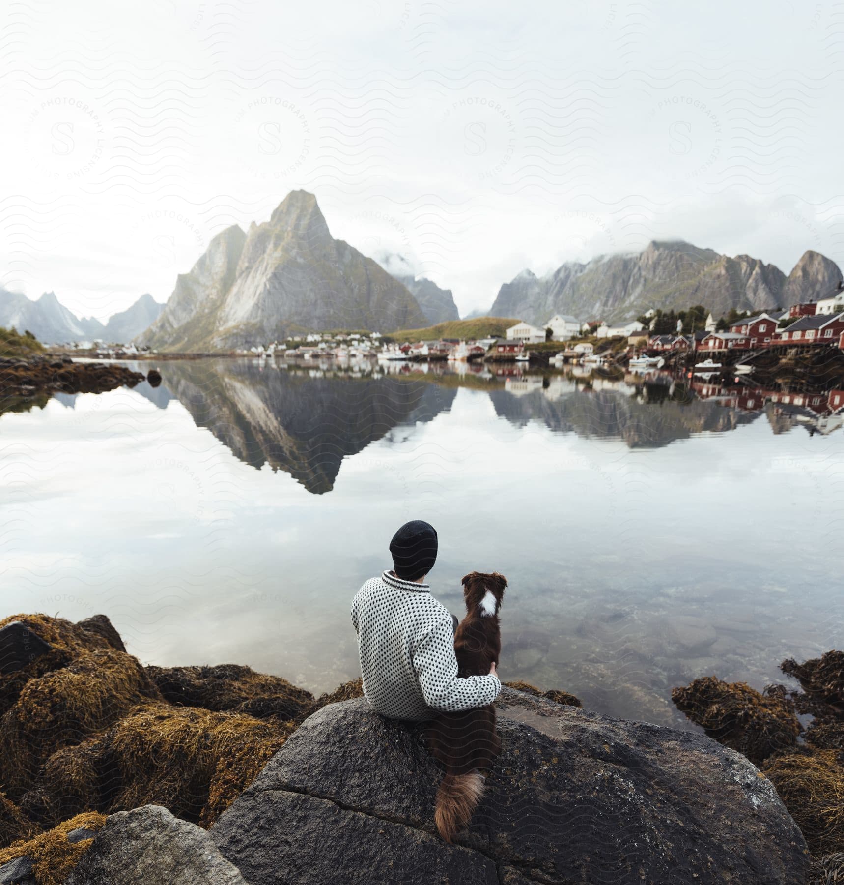 A man and his dog enjoying the scenic view of a lake surrounded by mountains in norway