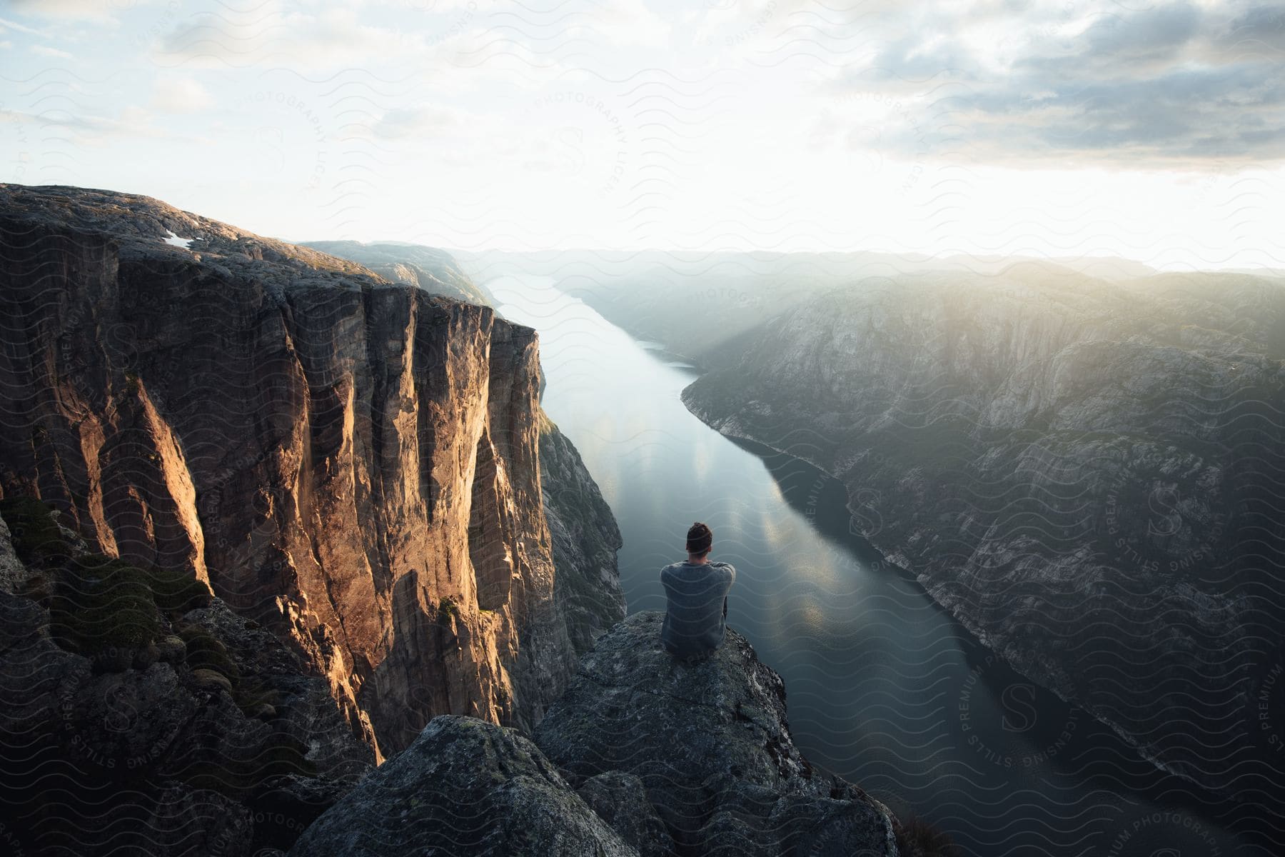 A young man sitting on the edge of a cliff looking at the sea