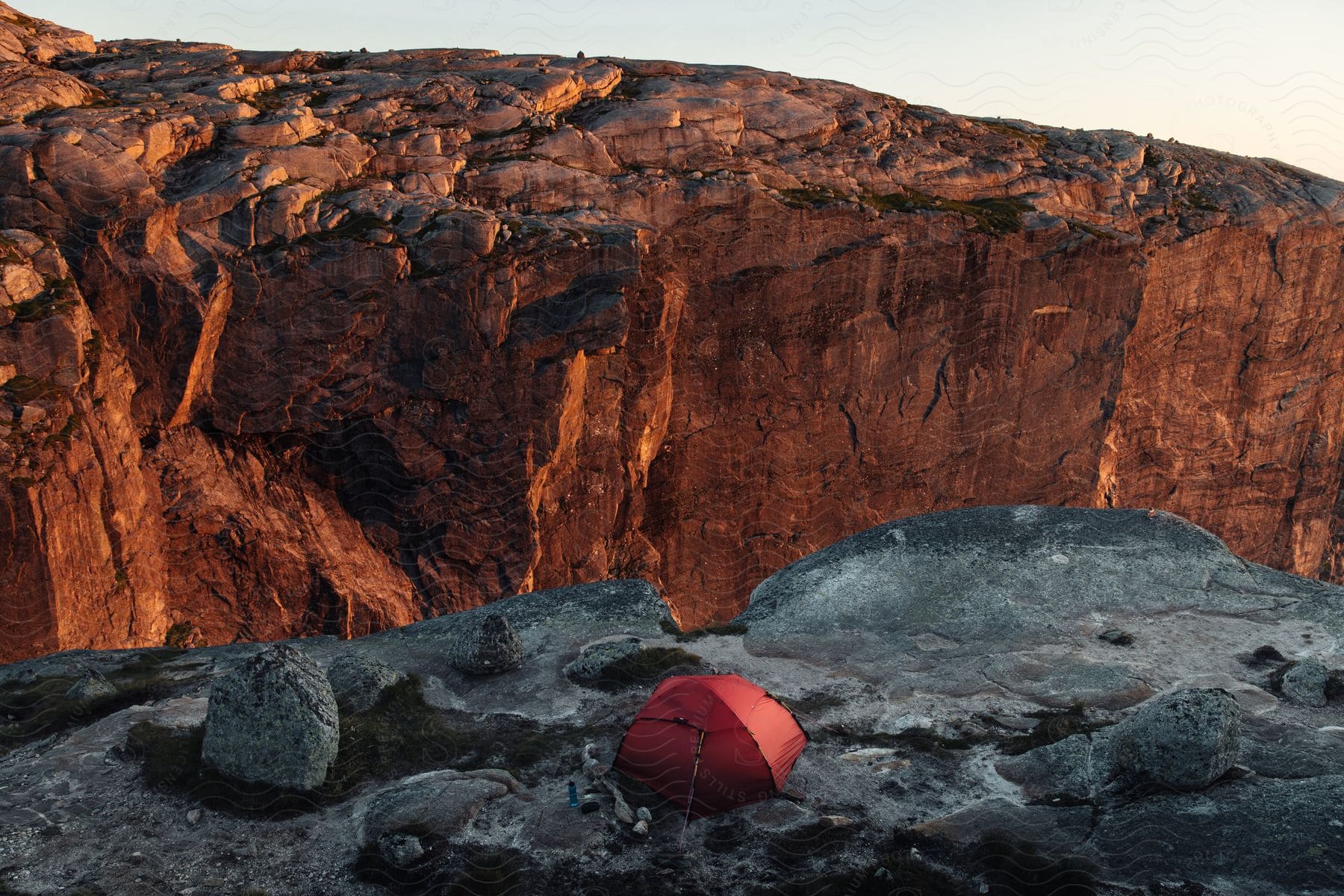 A red tent is perched on a cliff of black rocks overlooking a canyon