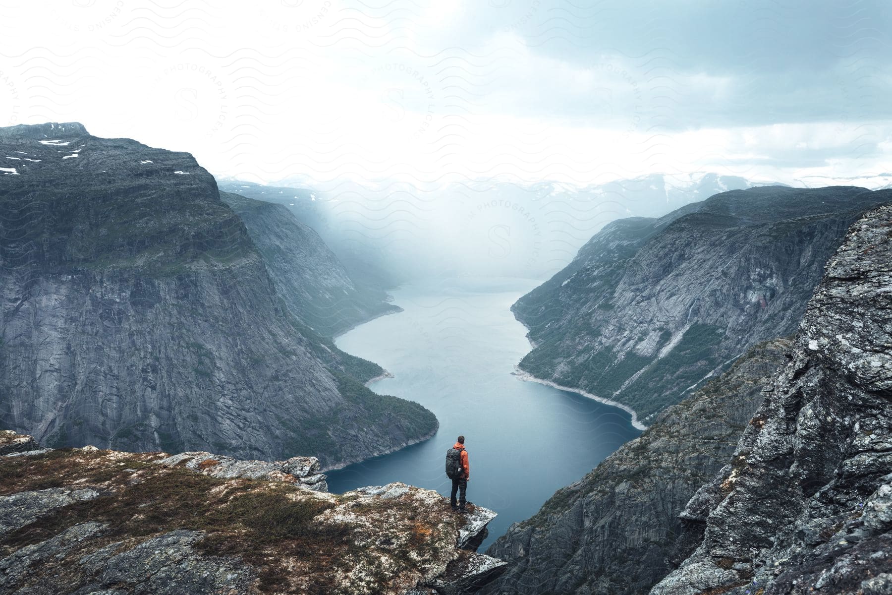 A man stands on the edge of a cliff overlooking a river in a rocky canyon