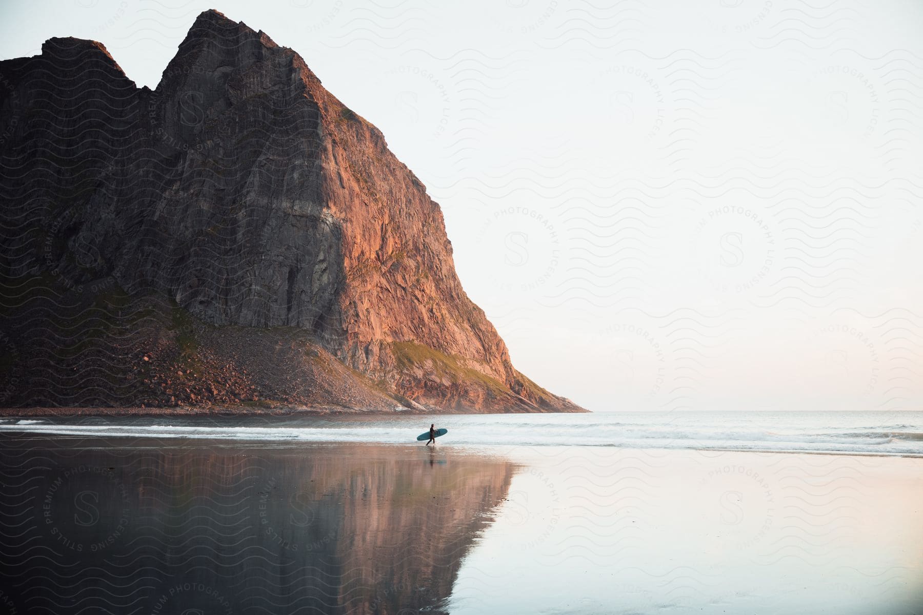 Wide shot of empty kvalvika beach with a person walking through carrying a surfboard