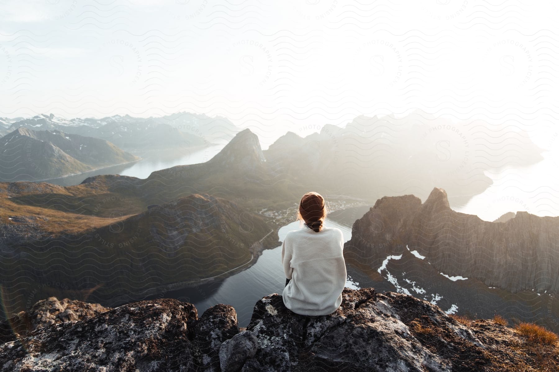 Woman sitting at mountain peak observing distant landscape