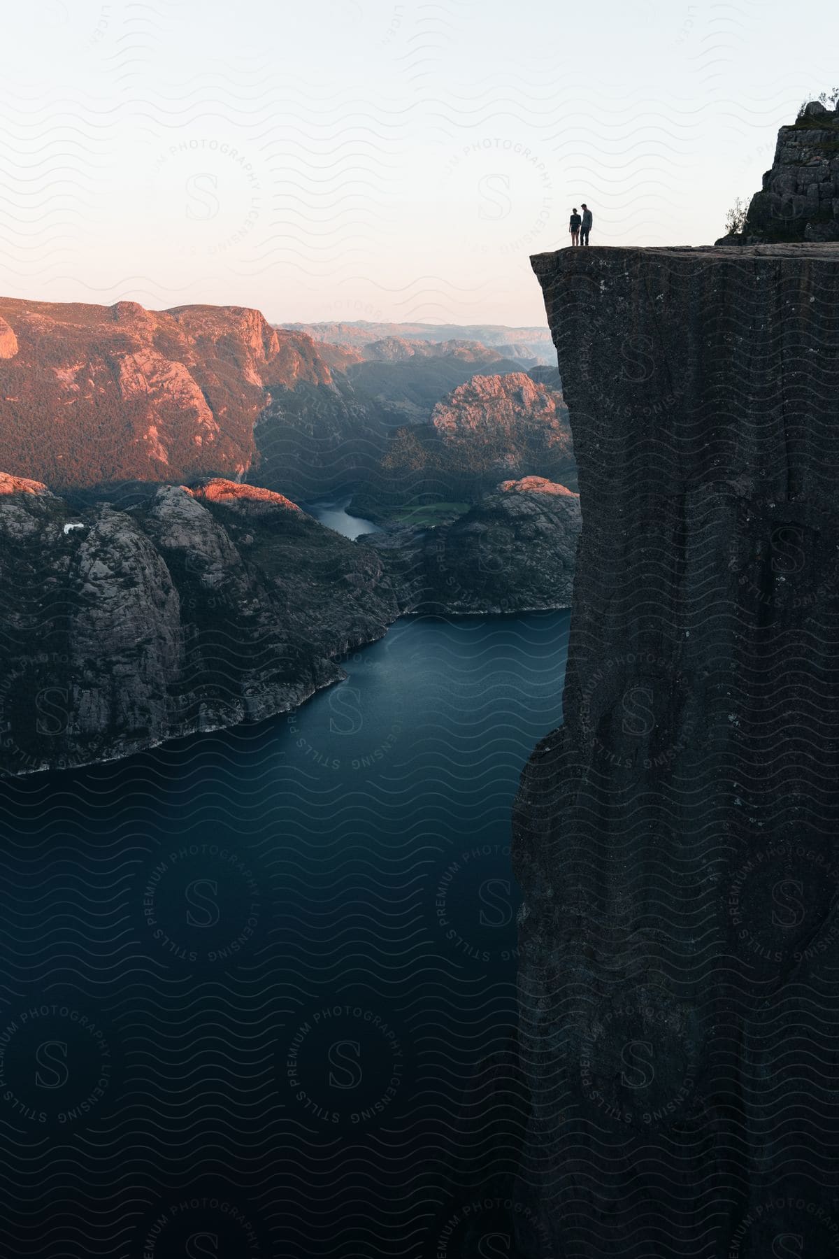Two people standing at the edge of preikestolen pulpit rock in norway at evening