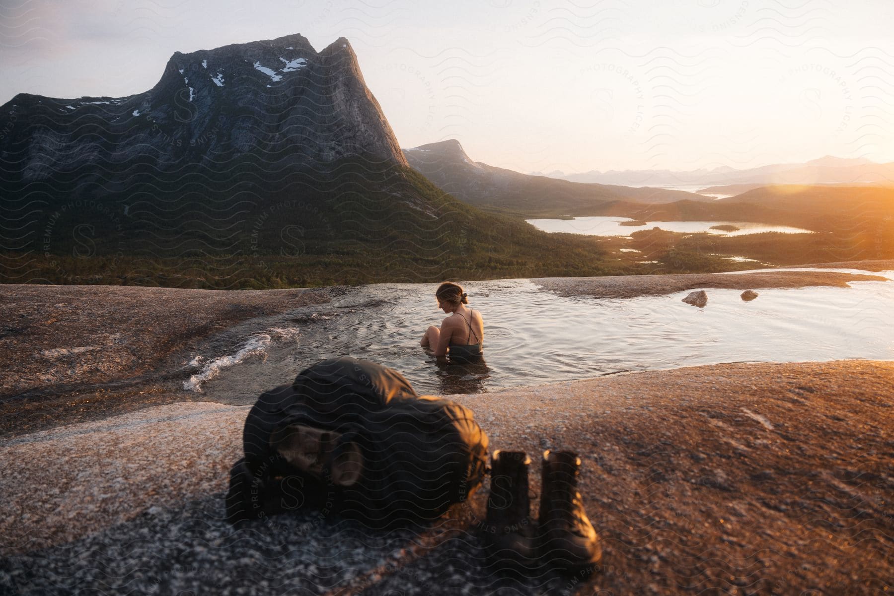 A woman sitting in a swimsuit in a pool on top of a rock enjoying the mountains