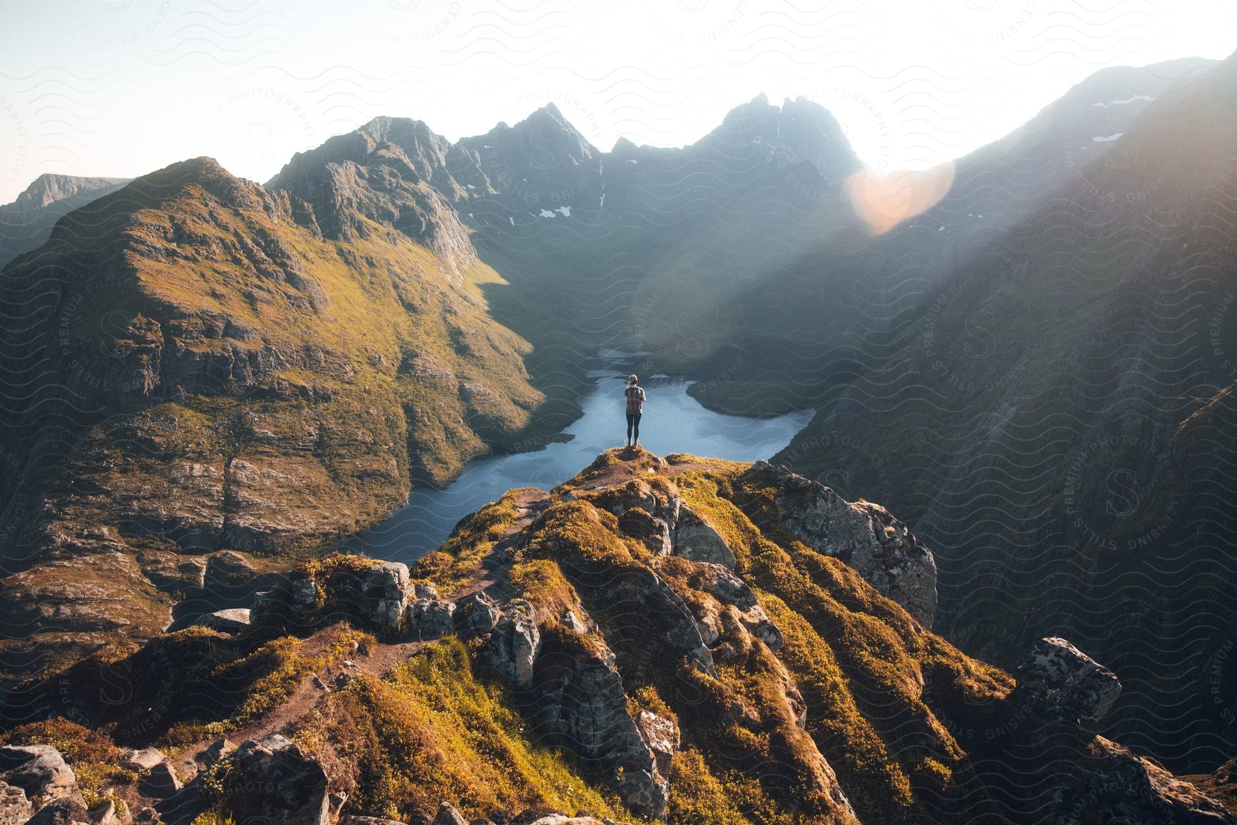 A man stands on a mountain overlooking a river valley with the sun shining upon him