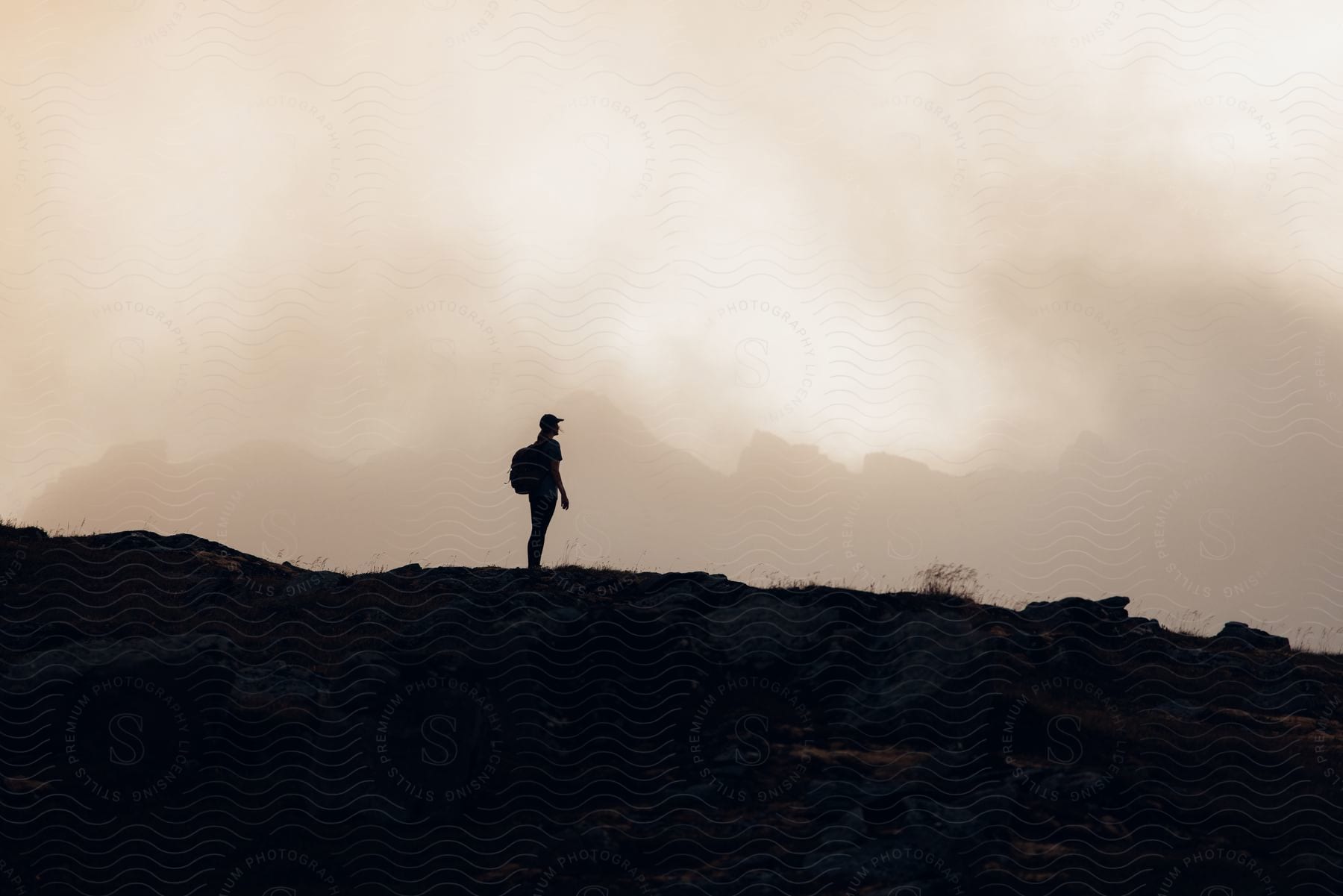 Stock photo of a person standing on a mountain slope with a cloudy sky in the background