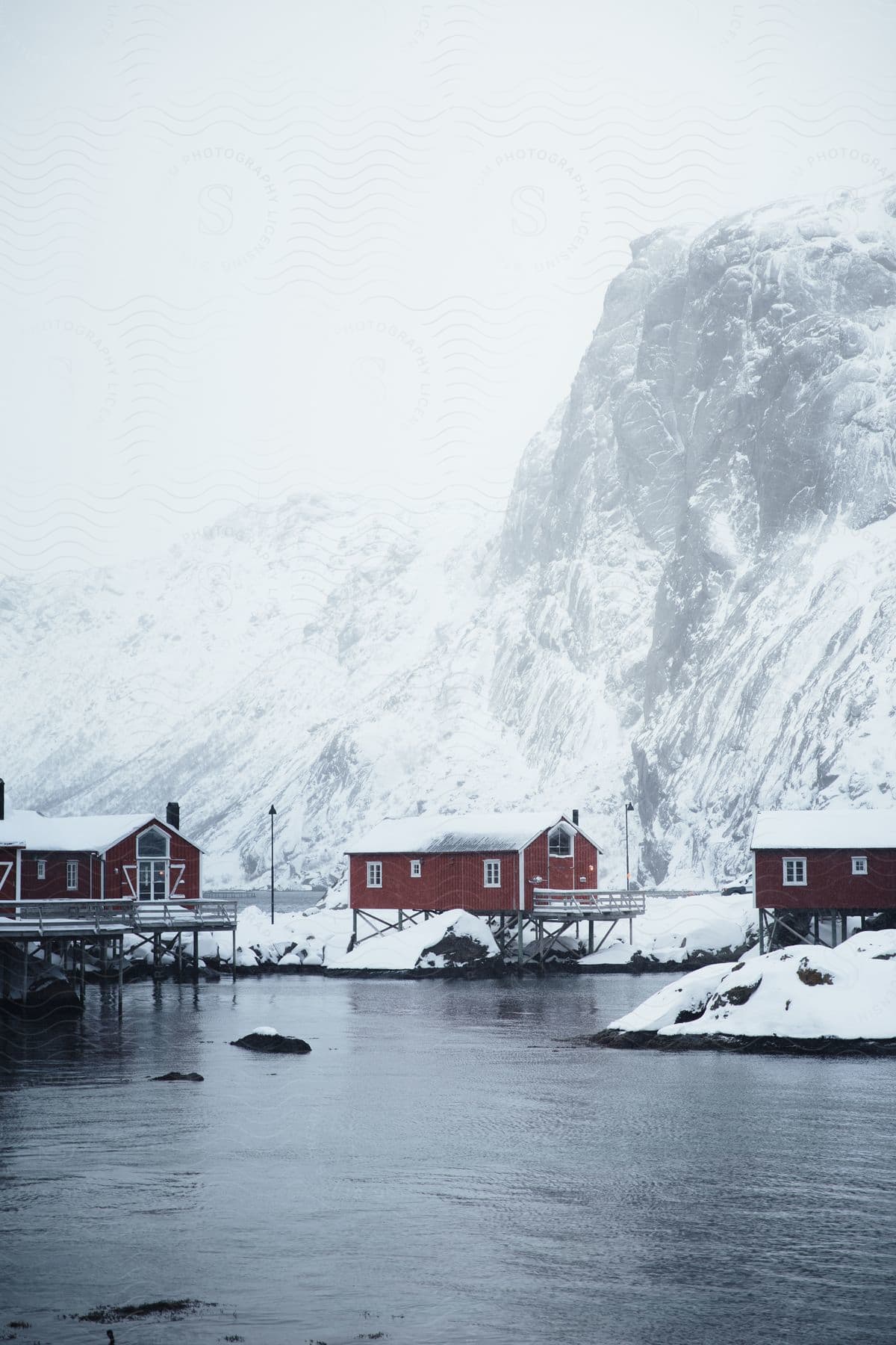 Red houses near high snowy mountains in fog on waterfront in norway winter