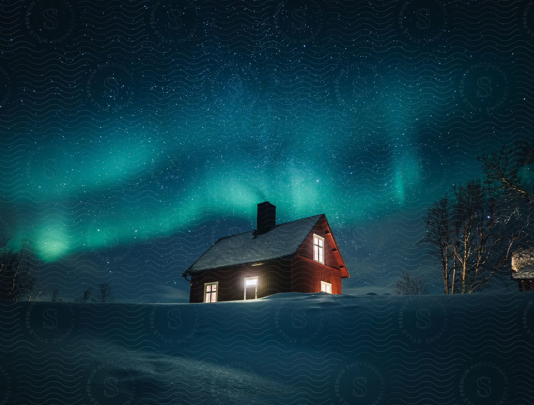 A house stands on snowcovered land with lights on under the glowing aurora borealis in the starry night sky