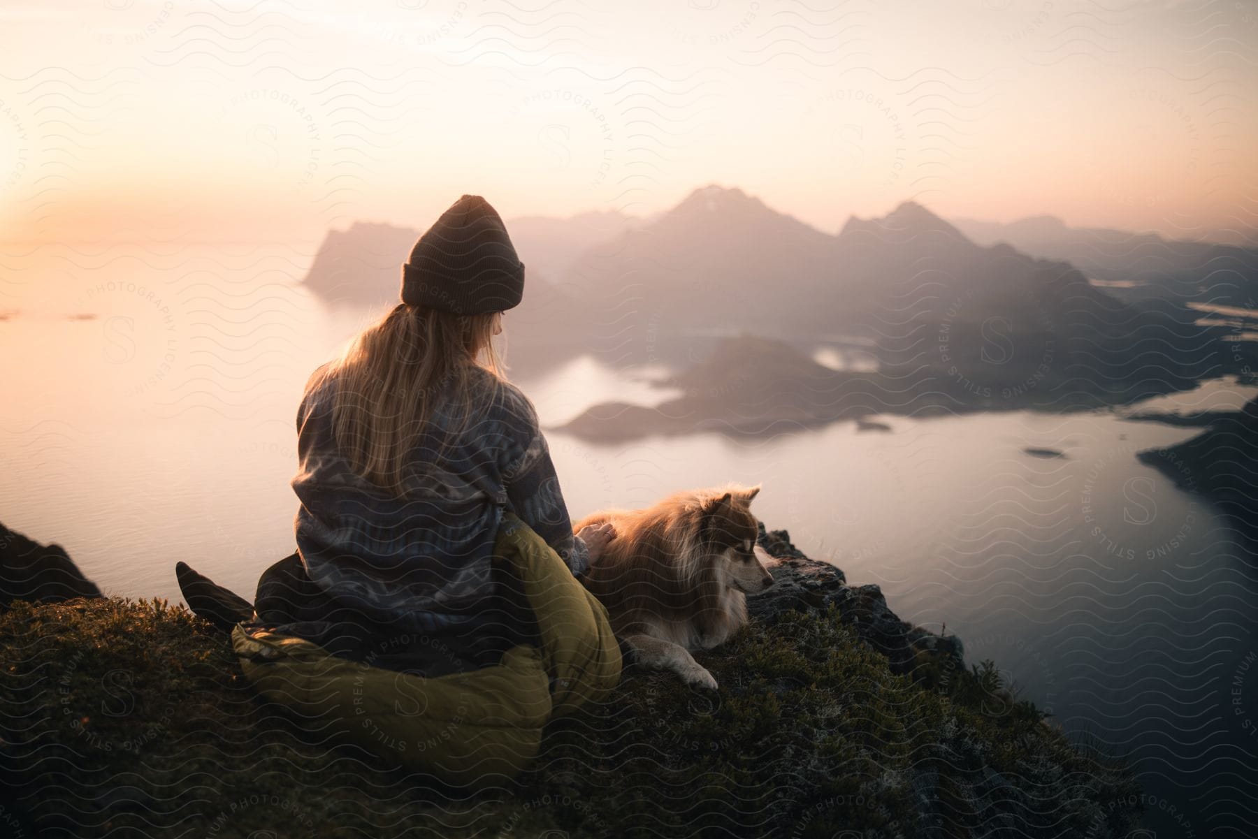 A young woman sits with her dog gazing at the ocean
