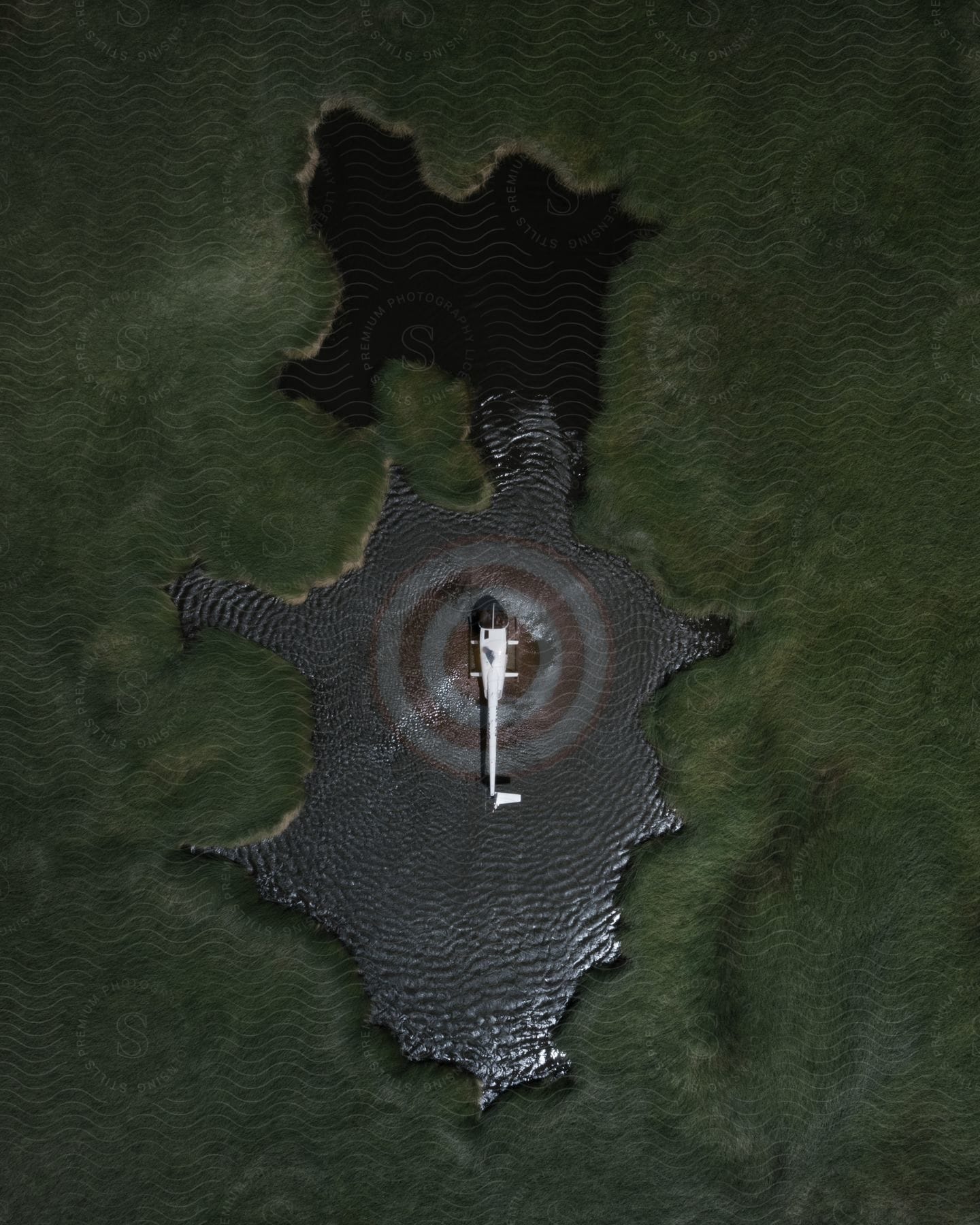 Stock photo of white helicopter landing on red target pad surrounded by water and forest