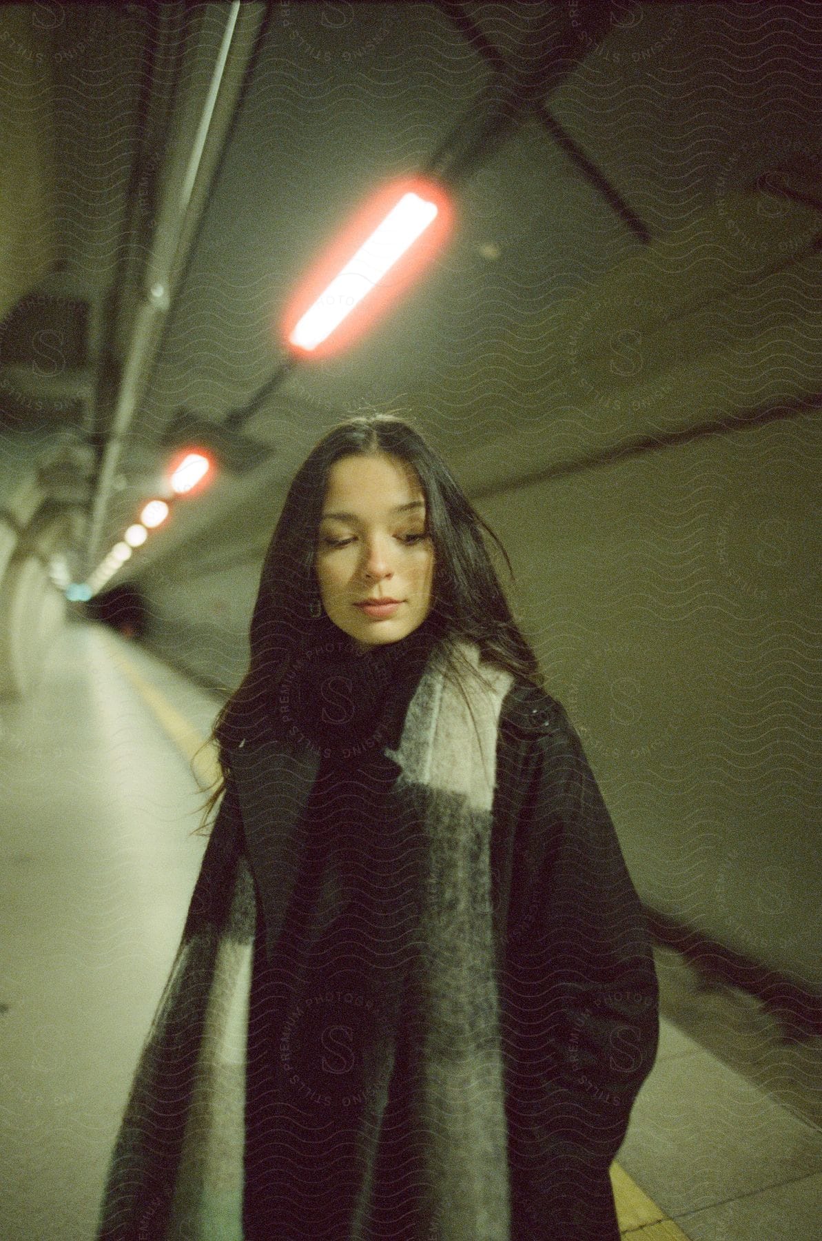 A darkhaired woman stands on a subway station at night